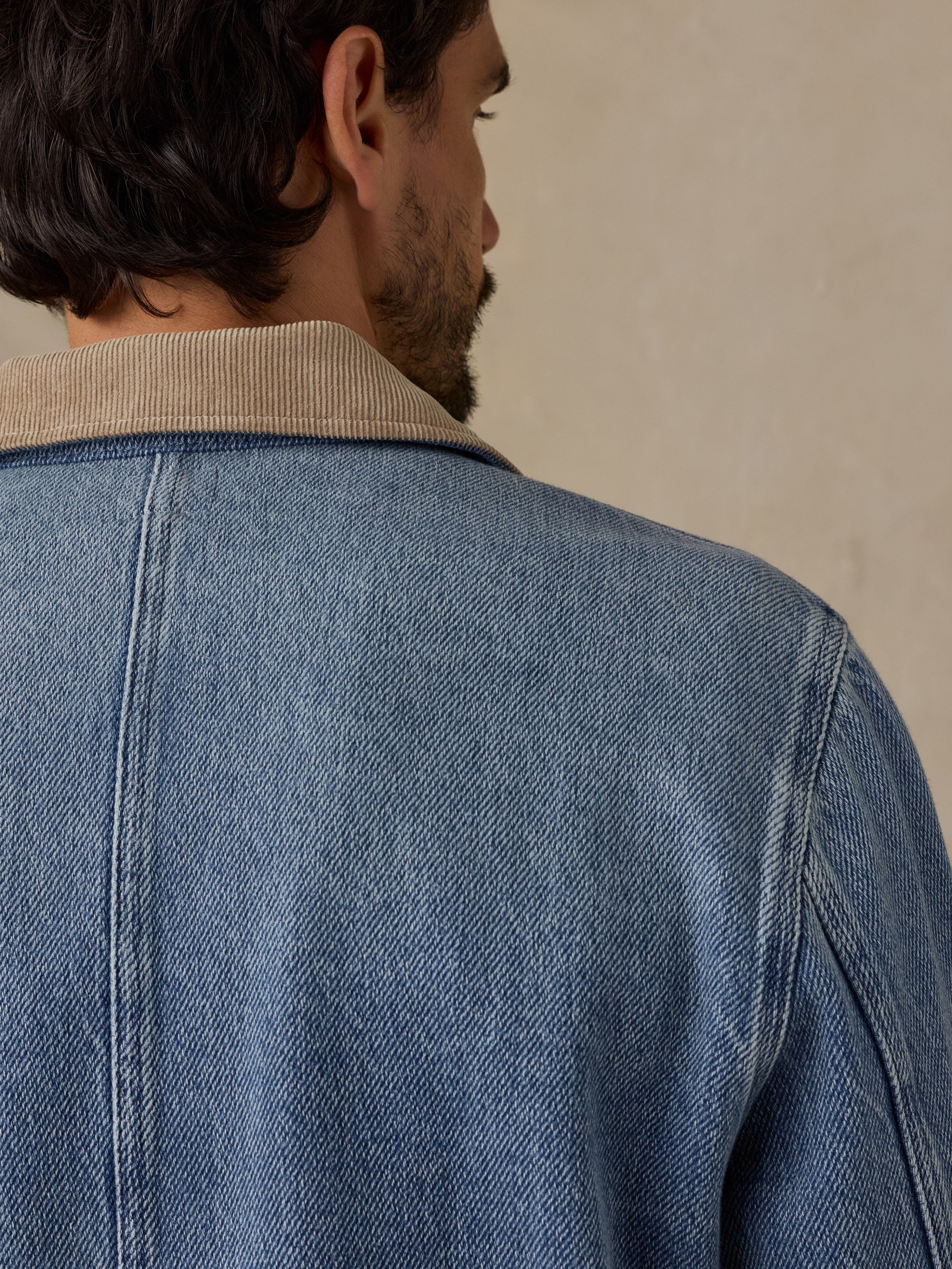 Man wearing a blue denim jacket with tan corduroy collar against a beige background