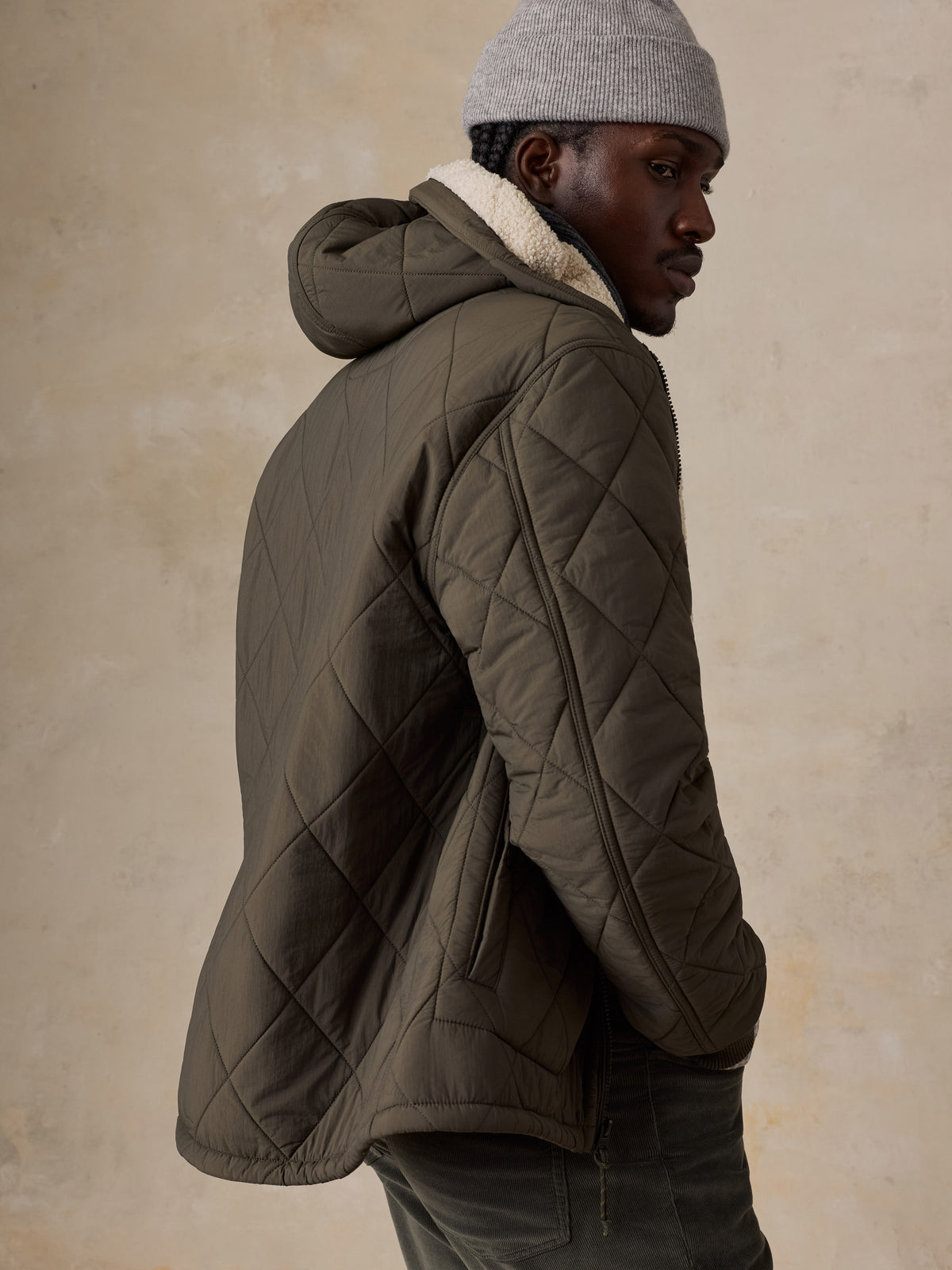 A man wearing a green quilted jacket and corduroy pants, image 4 of 5
