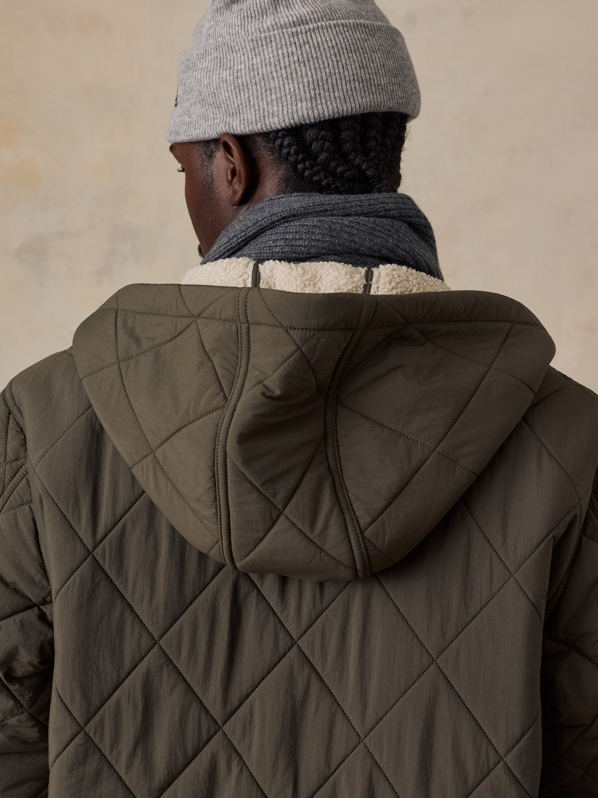 A man viewed from behind wearing a green quilted jacket and a grey beanie, image 5 of 5