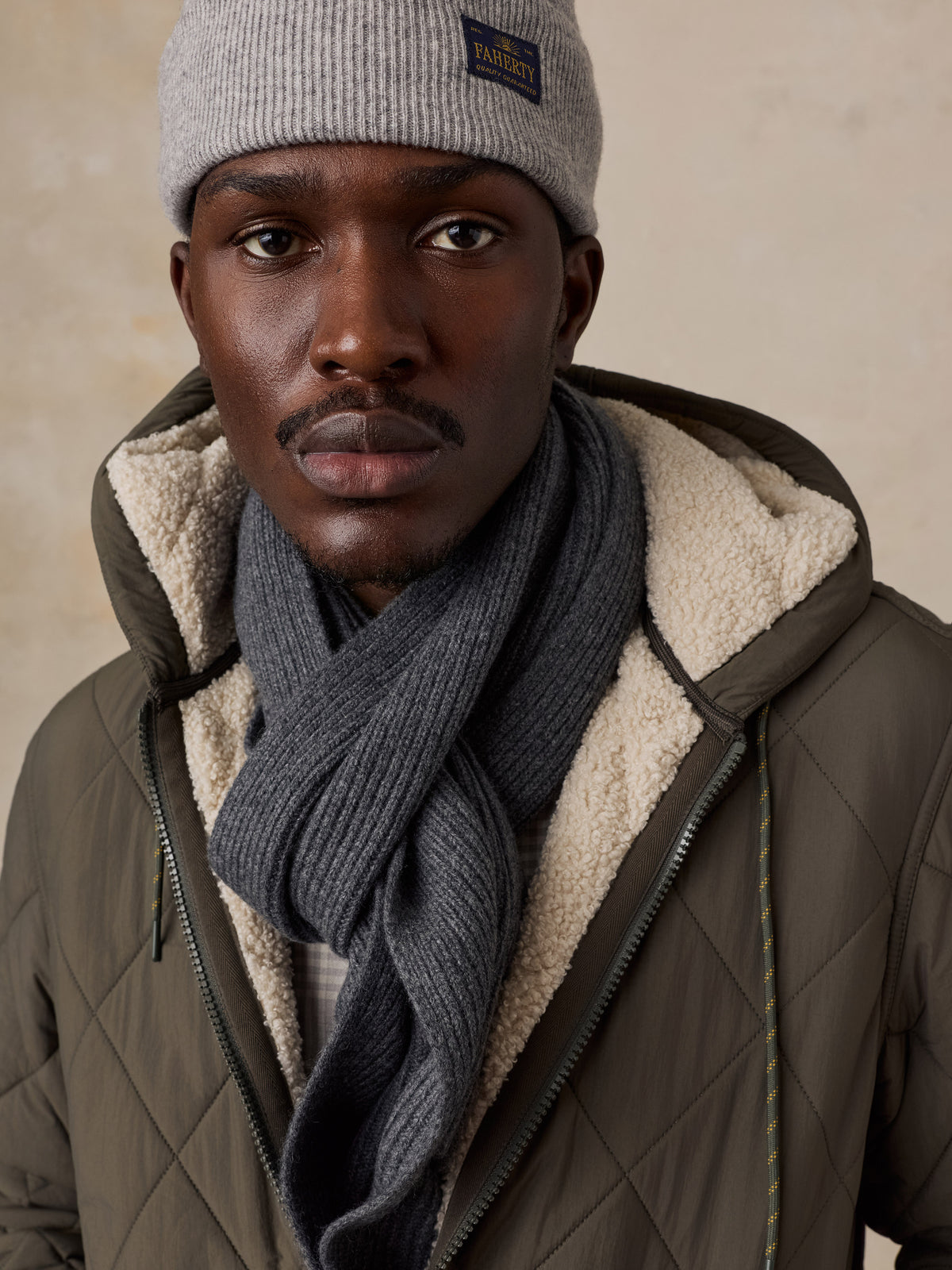 Close up of a man wearing a green quilted jacket with a grey scarf and beanie, image 3 of 5