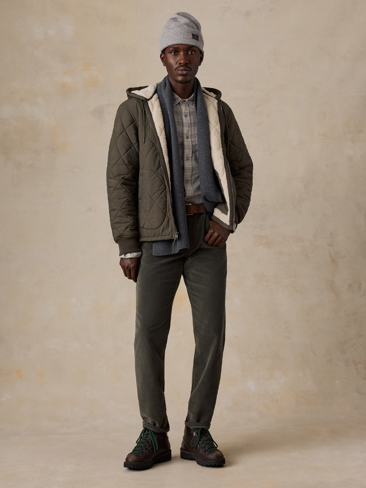 A man wearing a green quilted jacket over a plaid shirt and green corduroy pants, image 2 of 5
