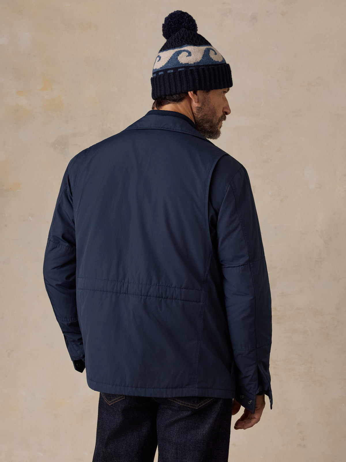 A man viewed from behind wearing a blue jacket and blue jeans, image 4 of 5