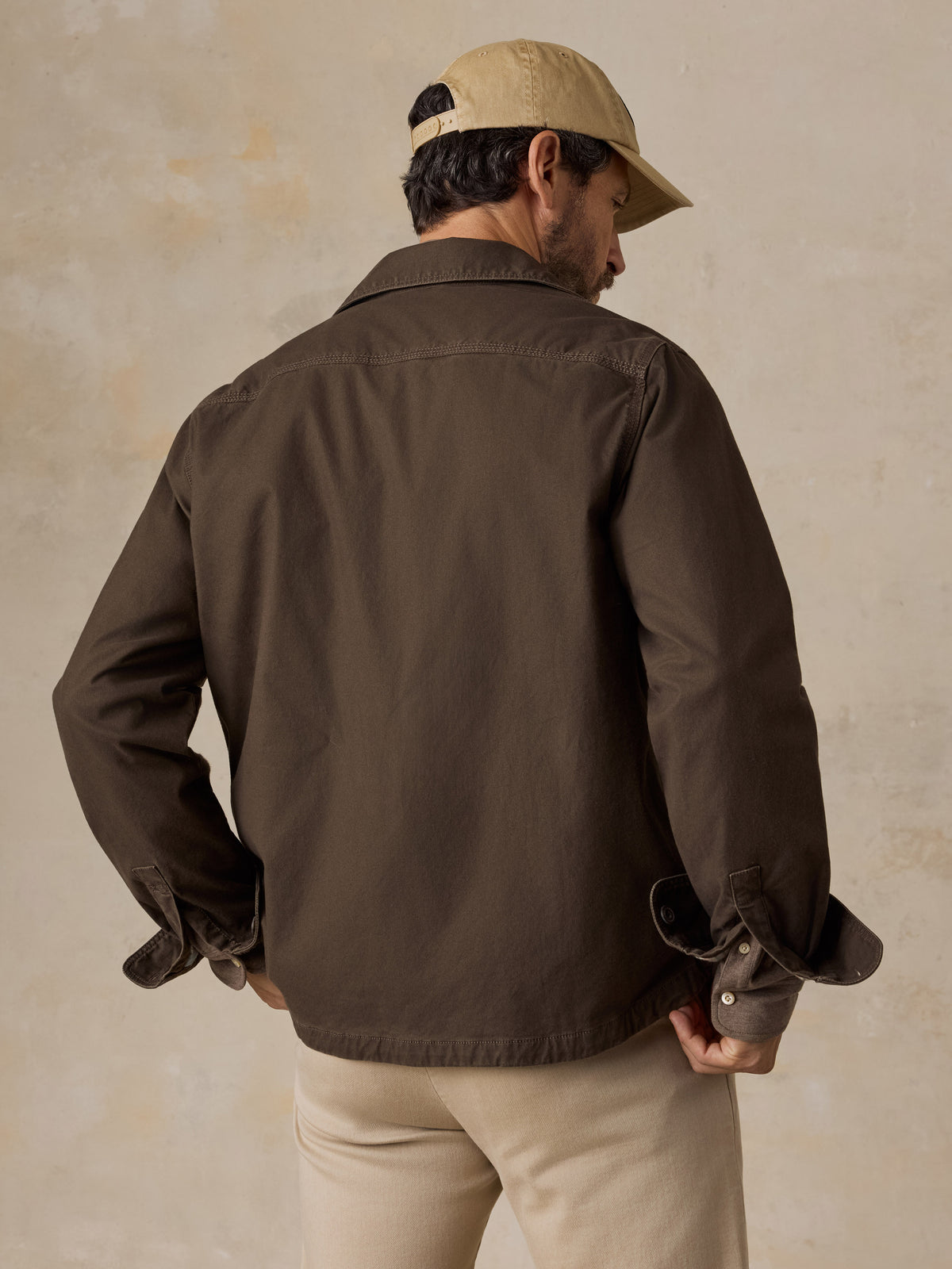 A man shown from behind wearing a brown jacket and beige pants, image 2 of 5