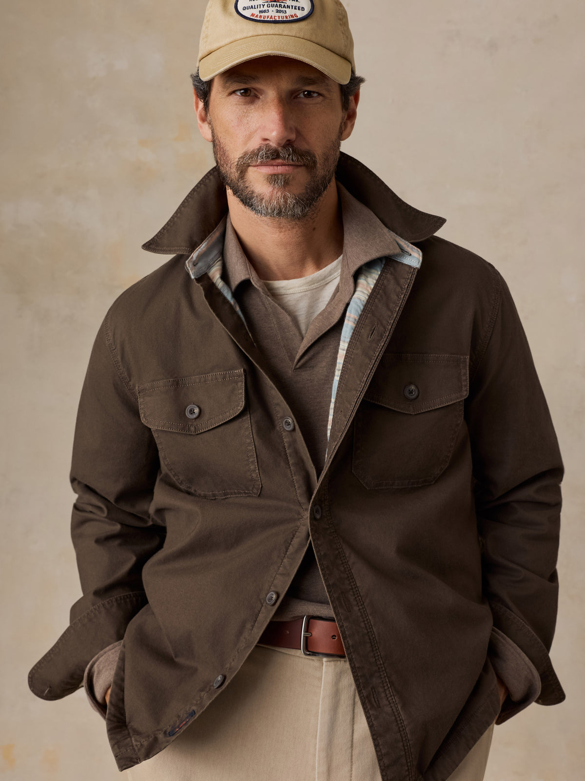 A man wearing a brown jacket over a brown polo and beige pants, image 4 of 5