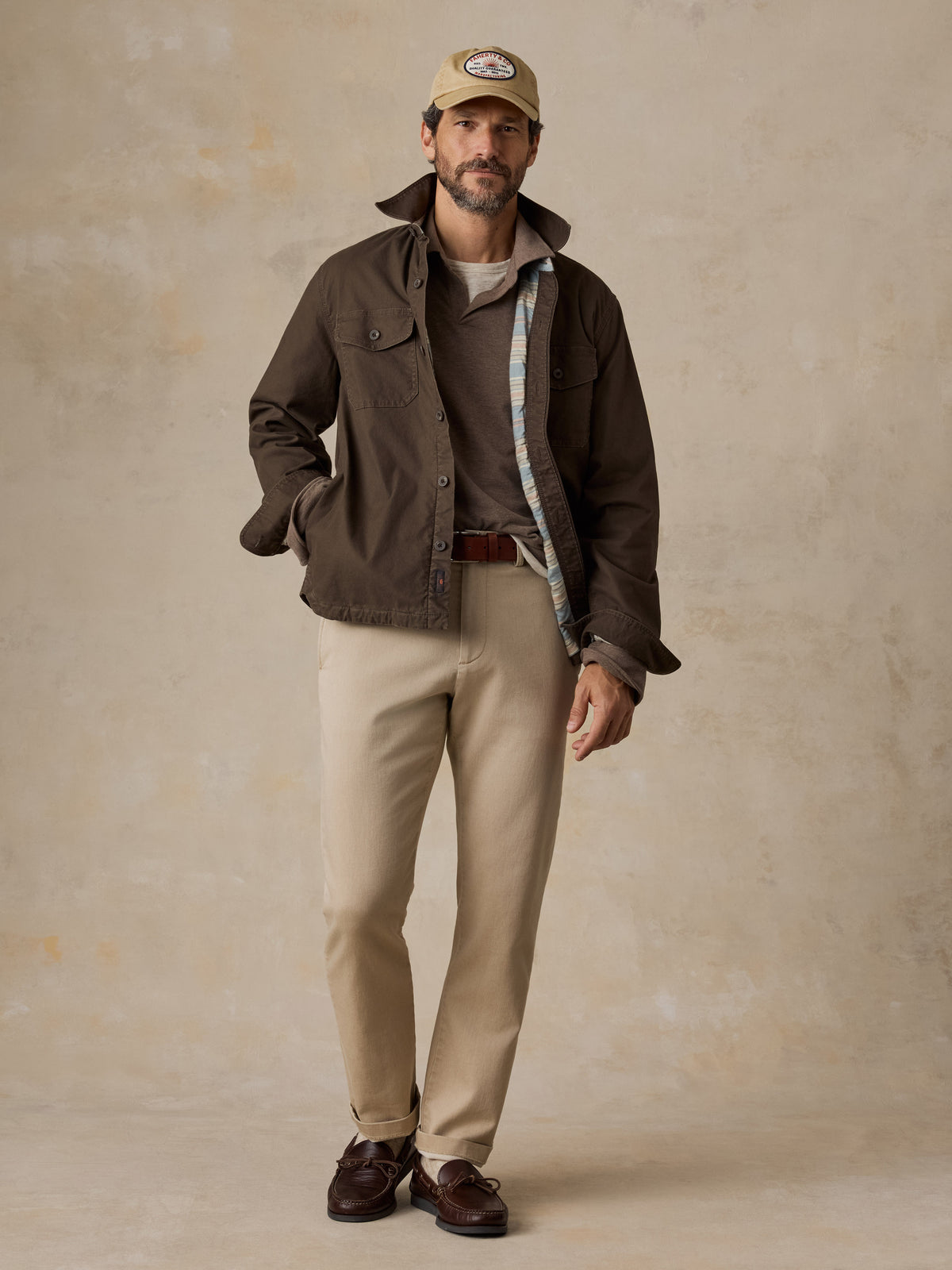 A man wearing a brown jacket over a brown polo and beige pants, image 5 of 5