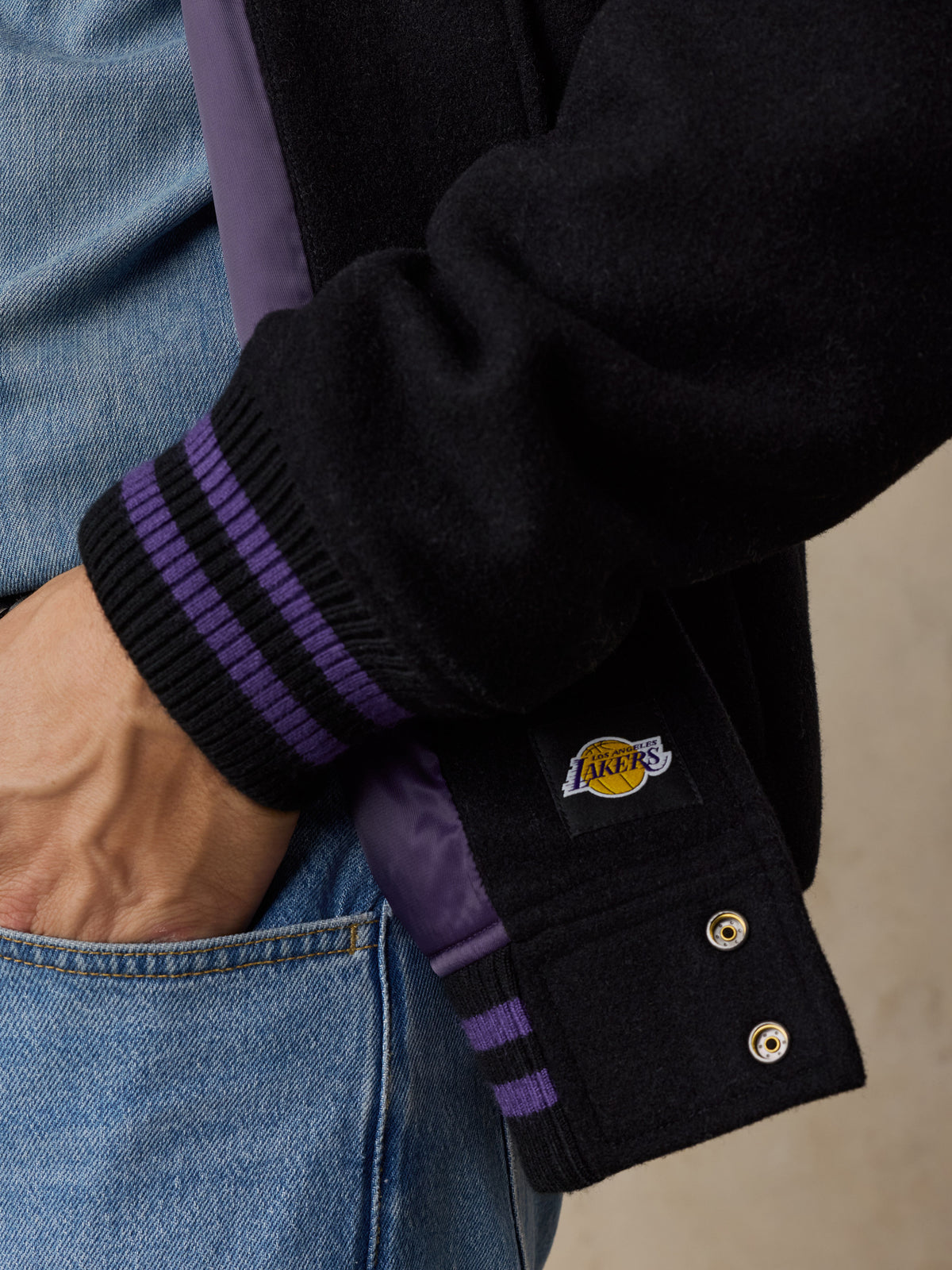 Close up of a man wearing a black LA Lakers varsity jacket and blue jeans, image 4 of 8