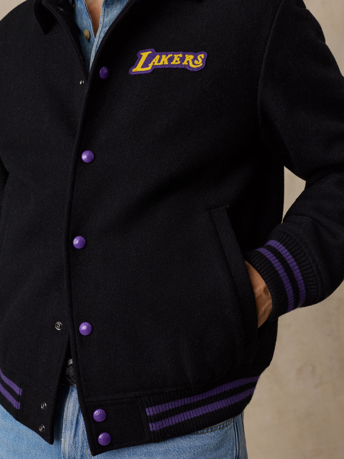 Close up of a man wearing a black LA Lakers varsity jacket and blue jeans, image 6 of 8