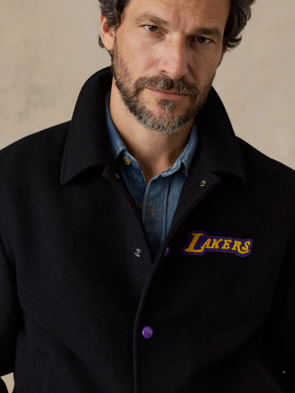 Close up of a man wearing a black LA Lakers varsity jacket and blue jeans, image 5 of 8