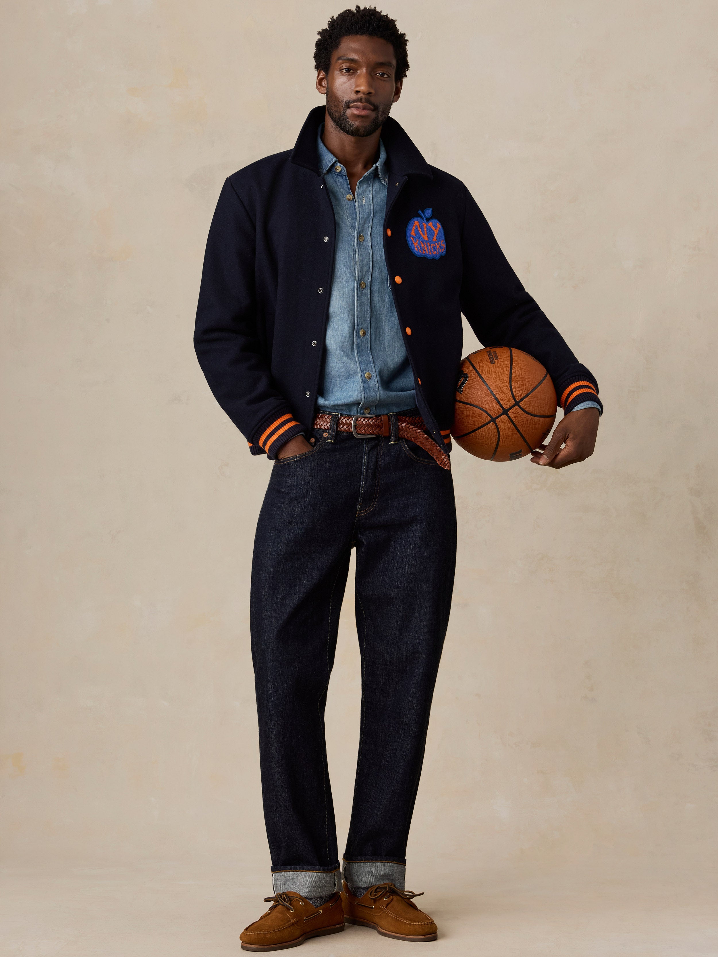 A man wearing a NY Knicks varsity jacket and jeans