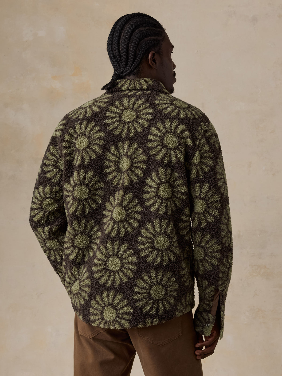 A man viewed from behind wearing a floral fleece jacket and brown pants, image 5 of 7