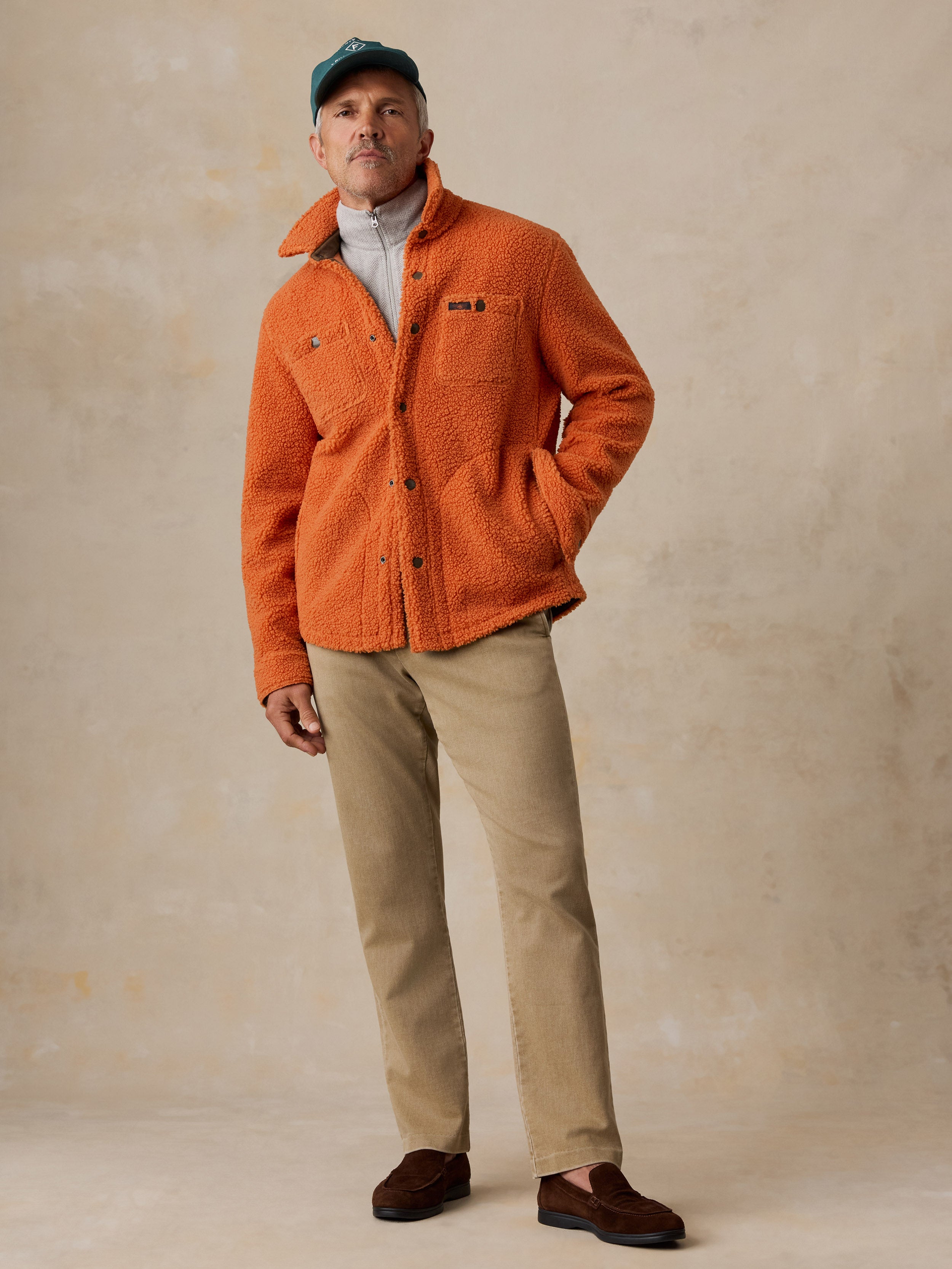A man wearing an orange fleece, chino pants, and loafers