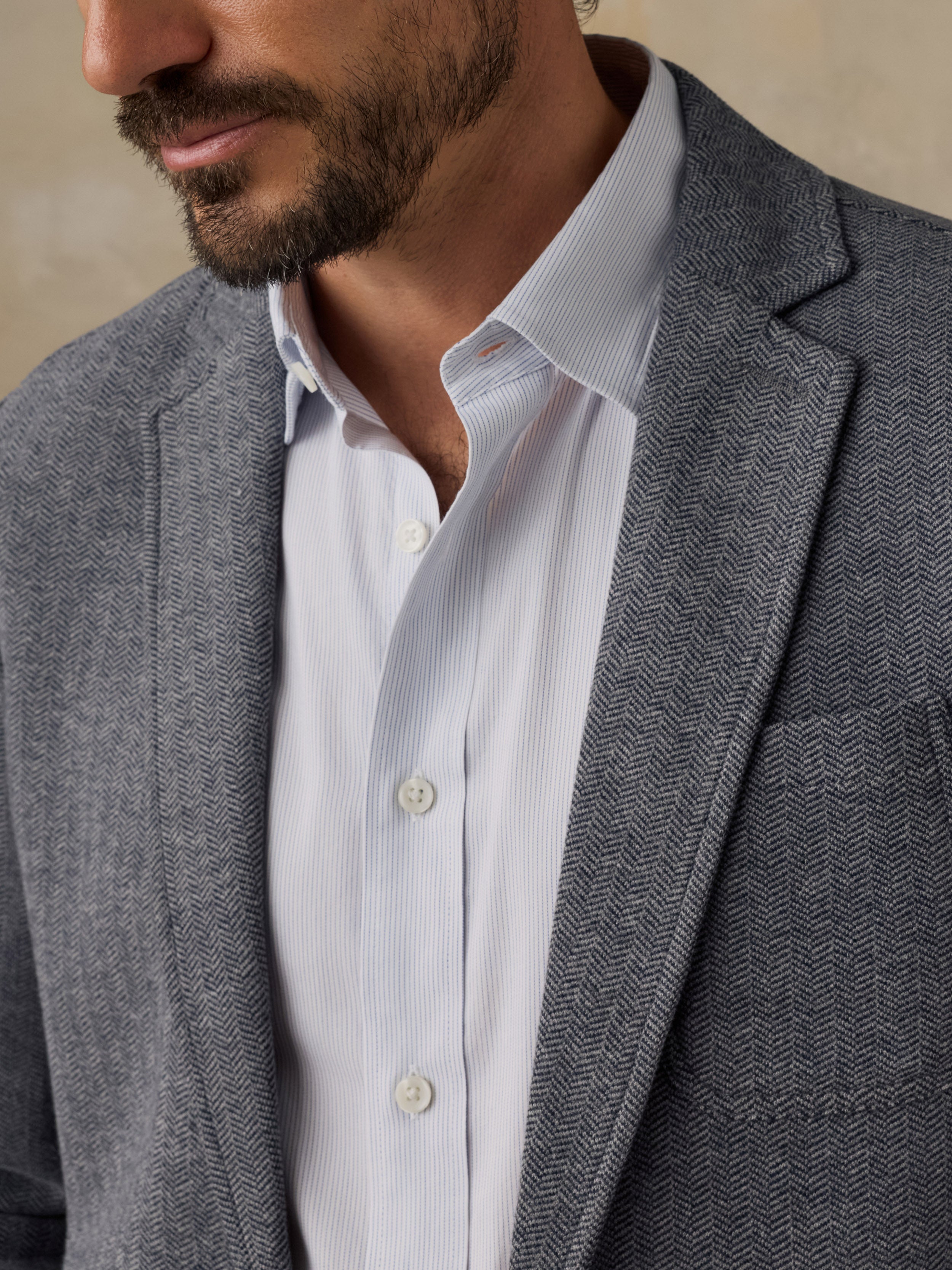 Close-up of a man wearing a gray tweed blazer over a white button-down dress shirt.
