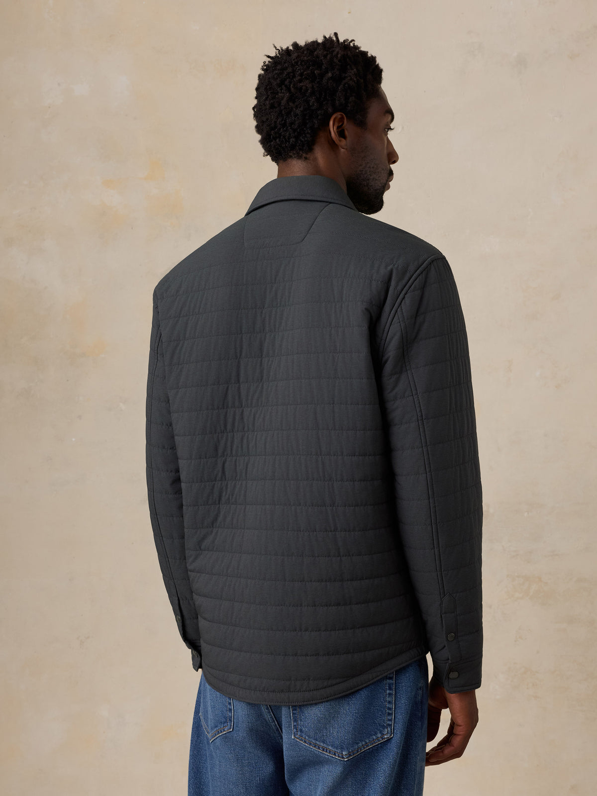 A man viewed from behind wearing a black jacket and jeans, image 4 of 4