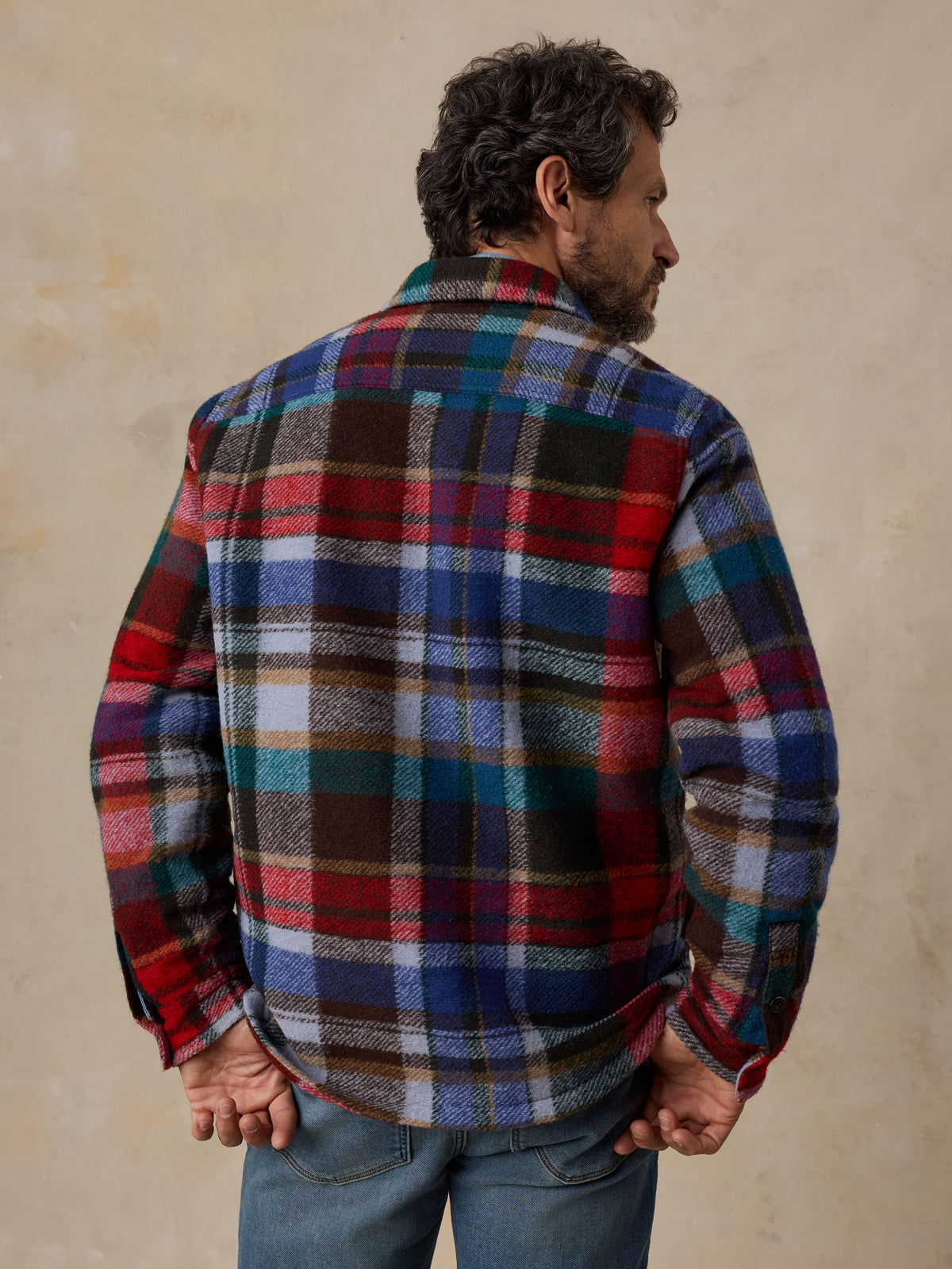 A man viewed from behind wearing a multicolored plaid jacket and jeans, image 4 of 6