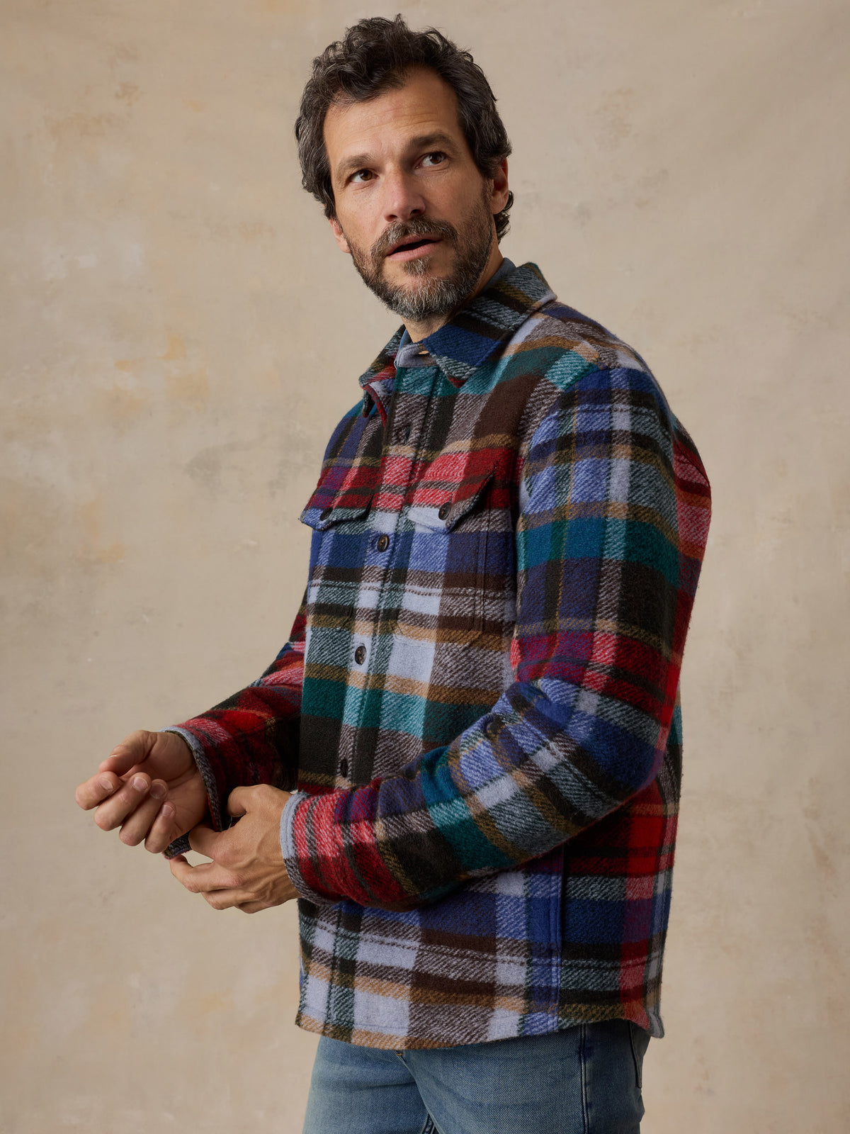 A man wearing a multicolored plaid jacket and jeans, image 6 of 6