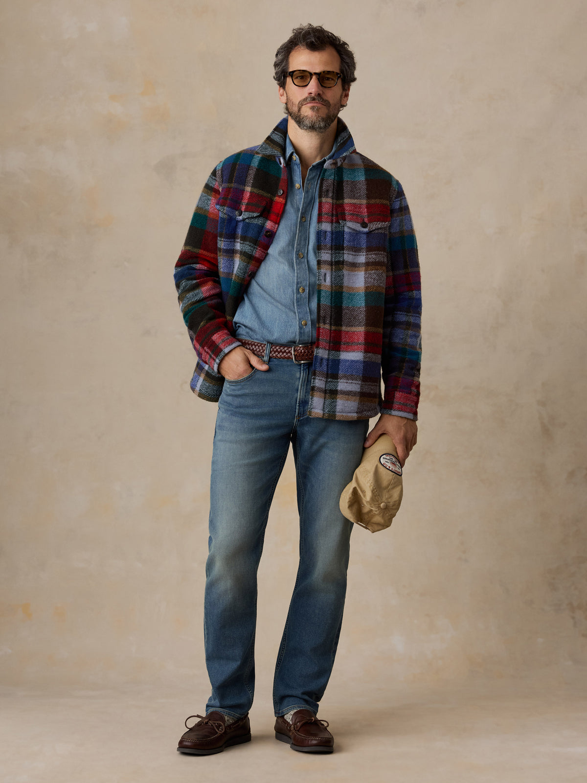 A man wearing a multicolored plaid jacket, jeans, and loafers, image 2 of 6