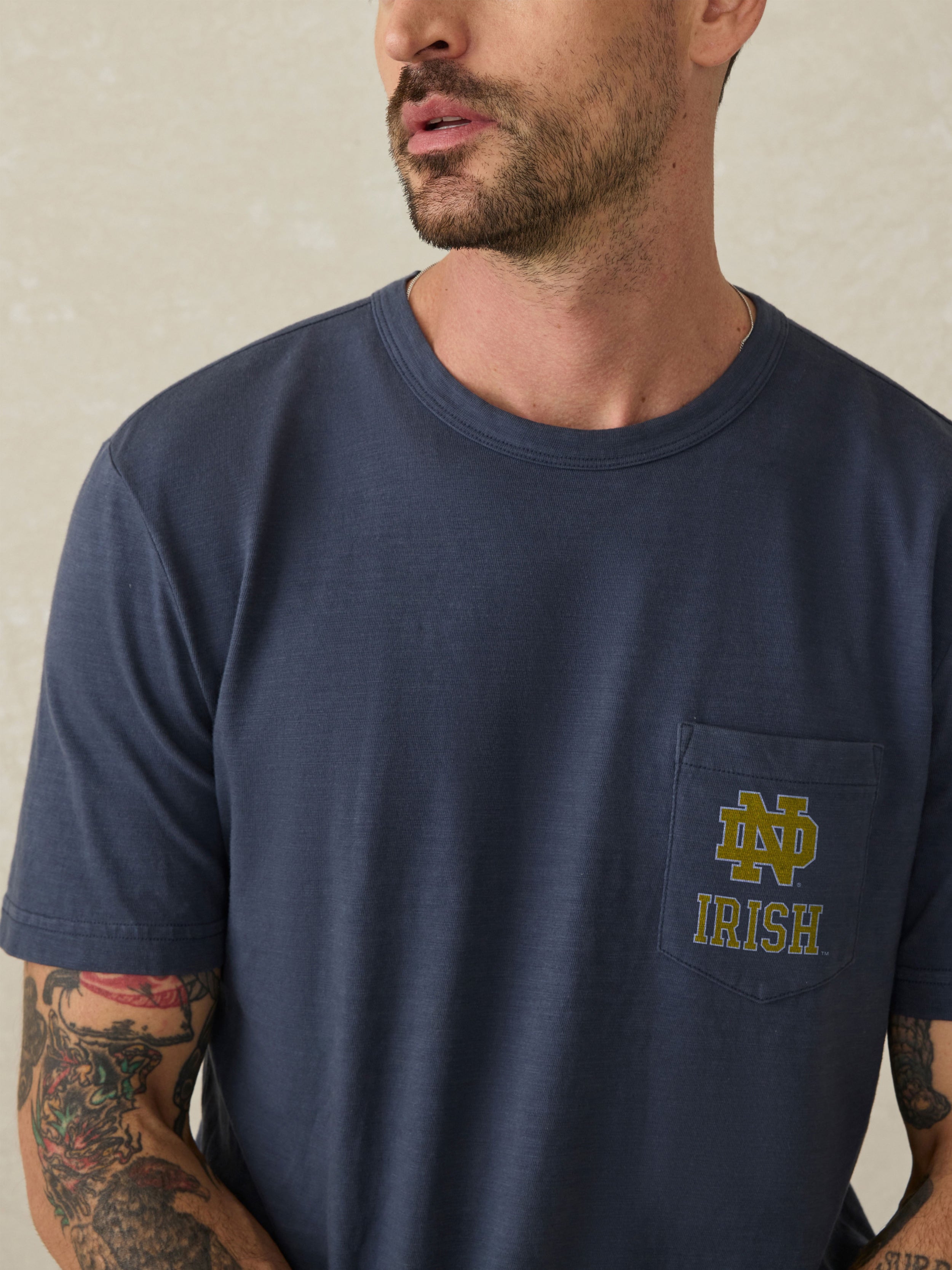 Man wearing a navy blue t-shirt with a Notre Dame logo on the chest against a beige background