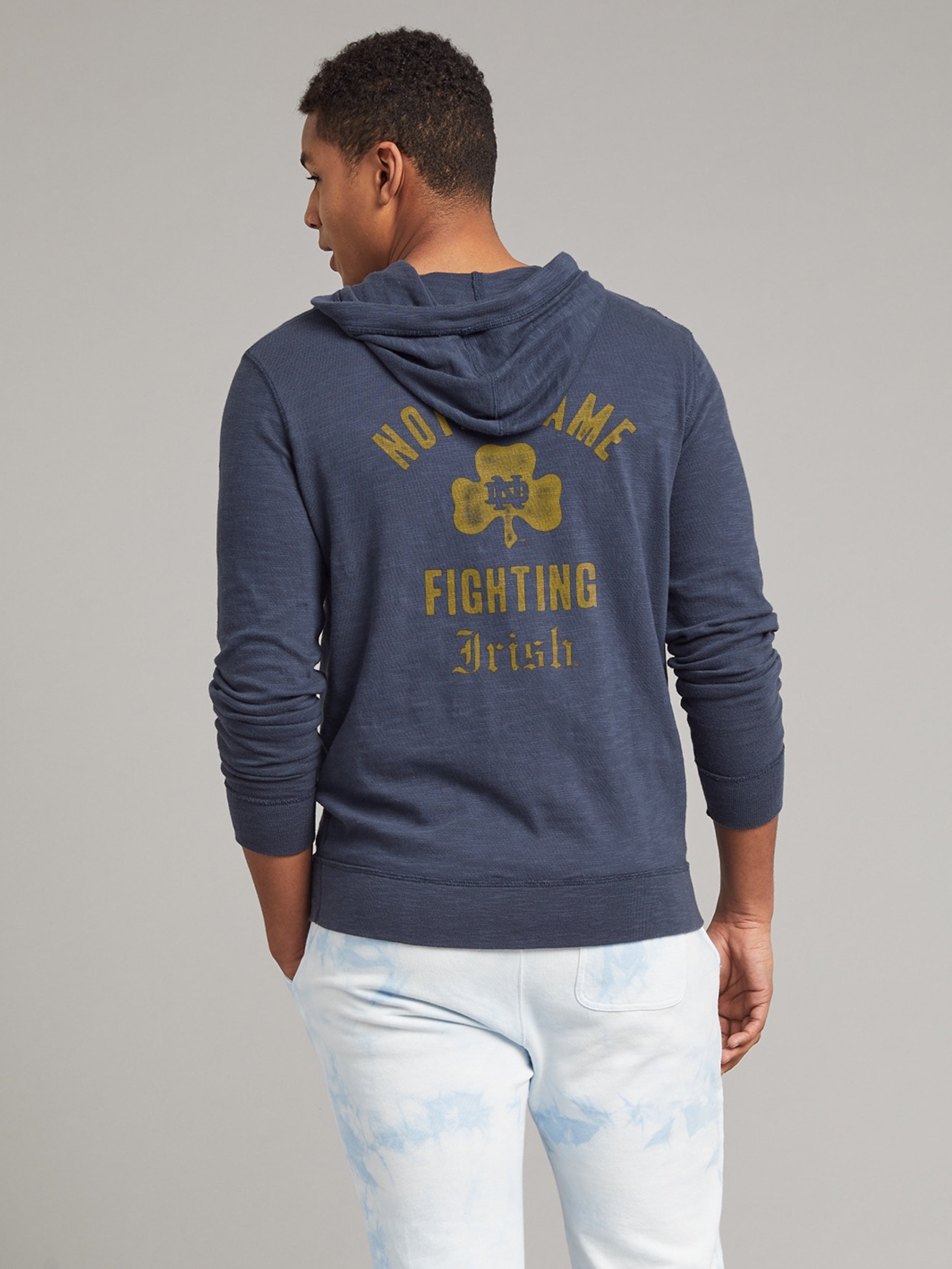Man wearing a navy hoodie with Notre Dame graphic on the center back against a grey background