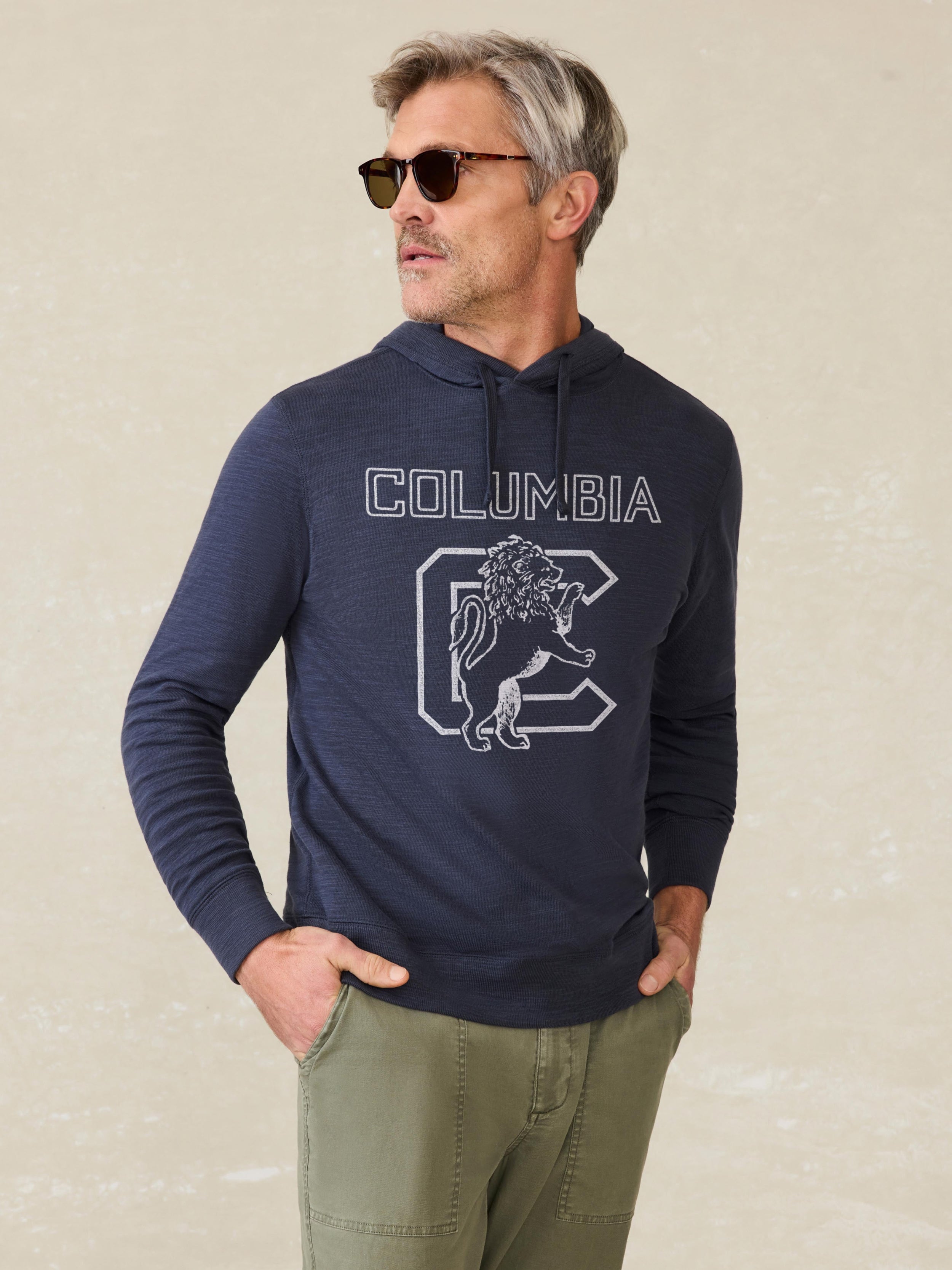 Man wearing a navy hoodie with Columbia graphic on the center front against a beige background