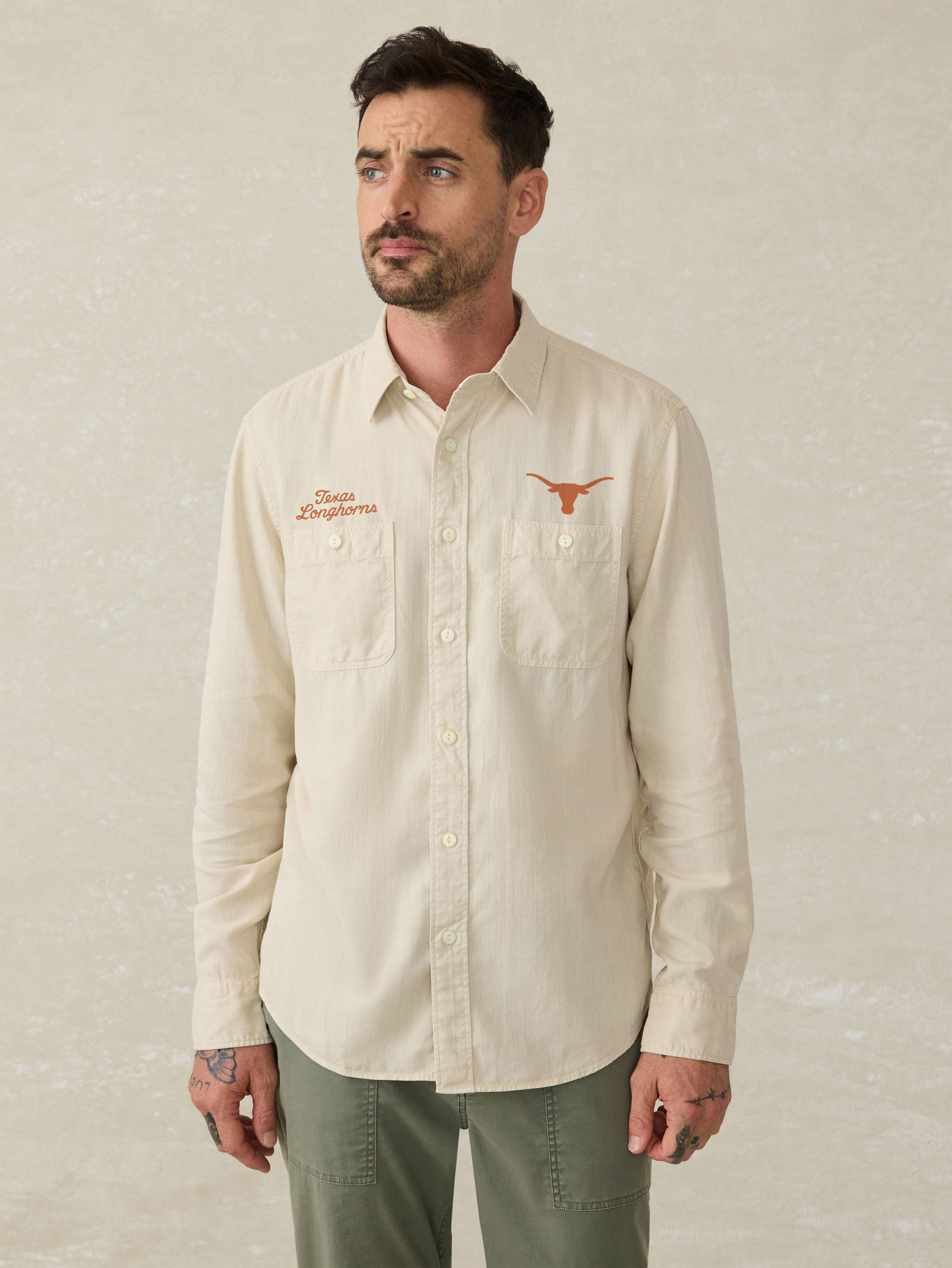 Man wearing an ivory long sleeve button down shirt with an University of Texas logo above the left and right chest pocket against a beige background