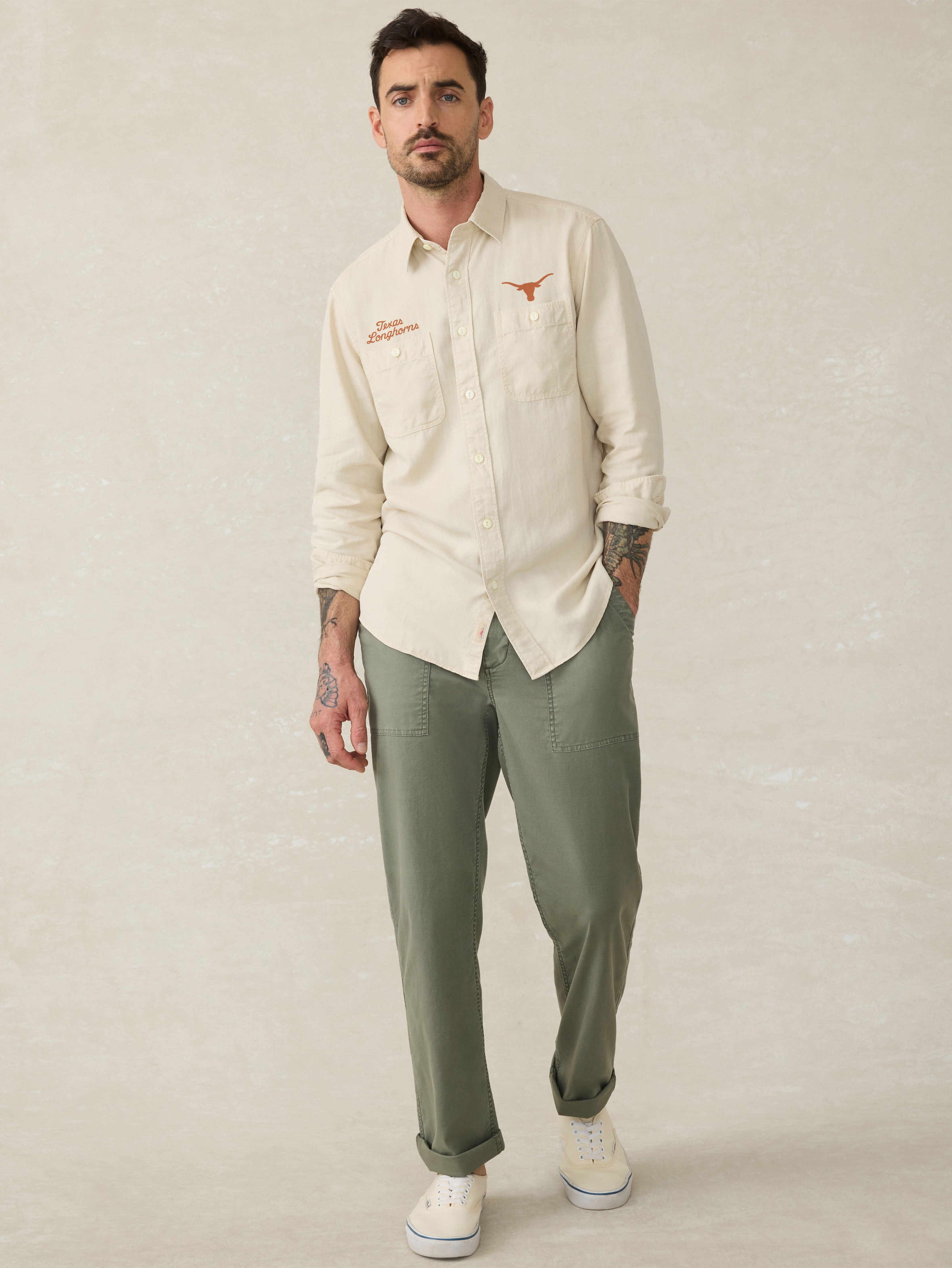 Man wearing an ivory long sleeve button down shirt with an University of Texas logo above the left and right chest pocket against a beige background
