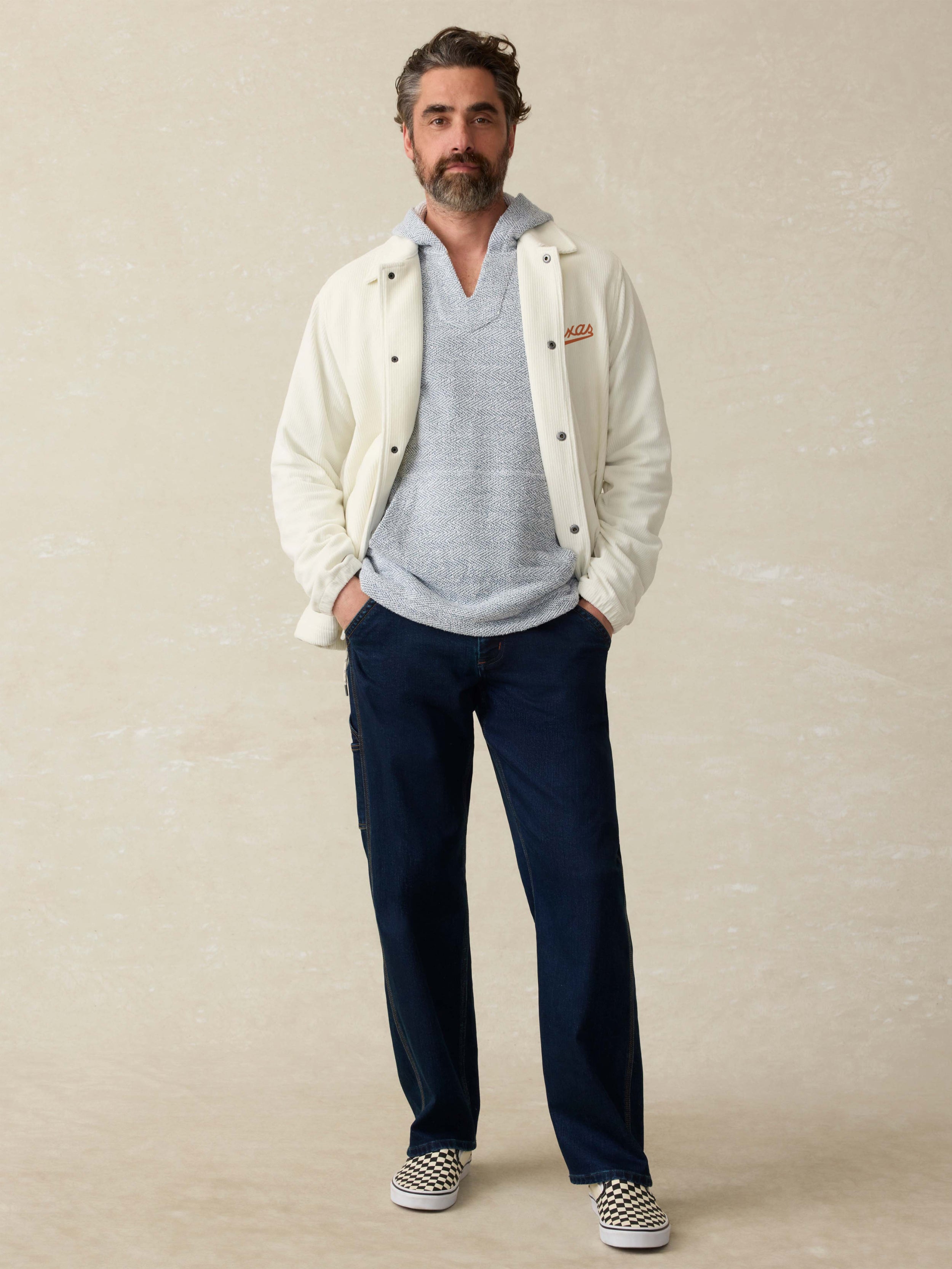 Man is wearing a white coaches jacket with UT Austin graphic on the left chest against a beige background