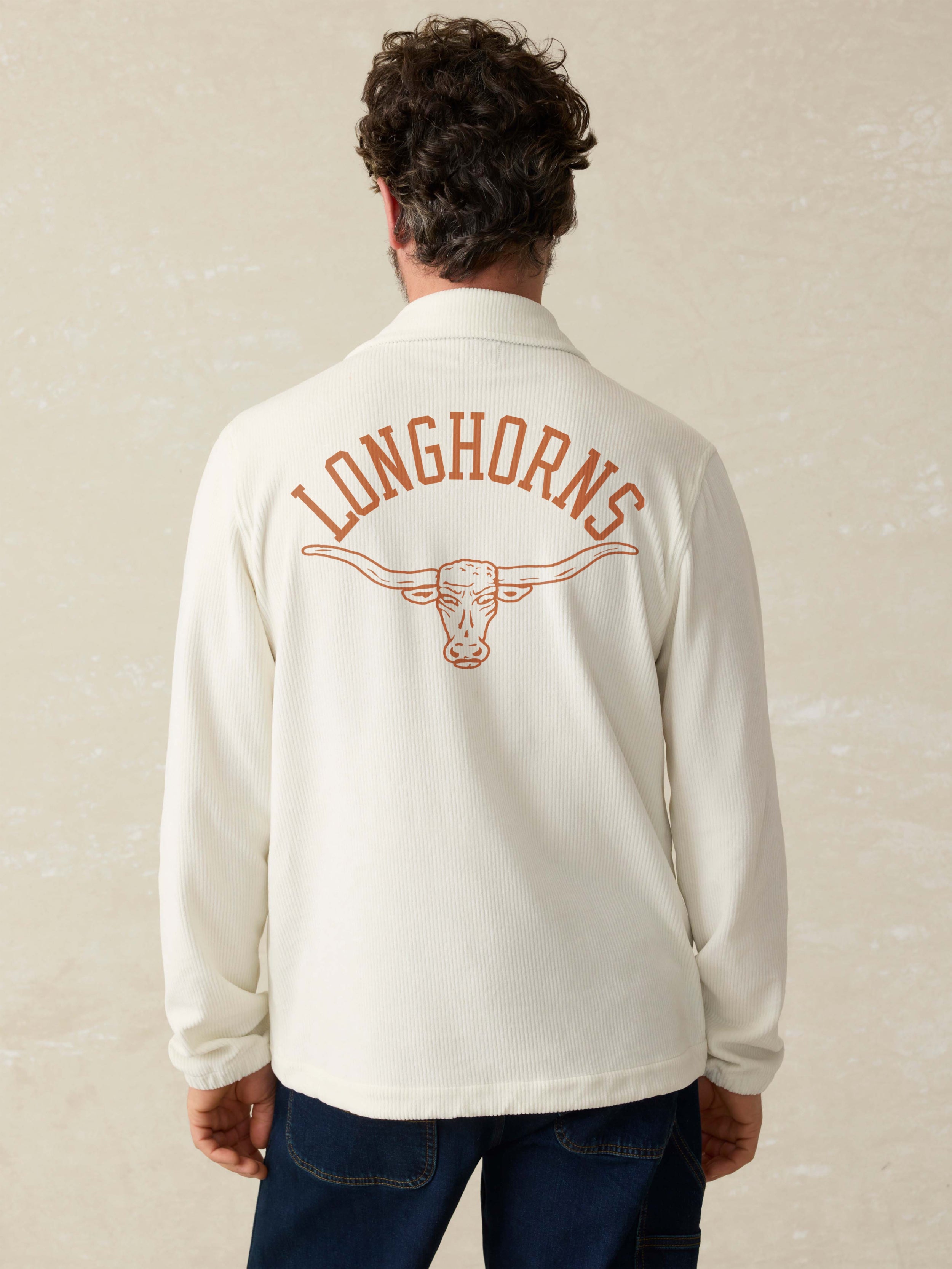 Man is wearing a white coaches jacket with UT Austin graphic on the center back against a beige background