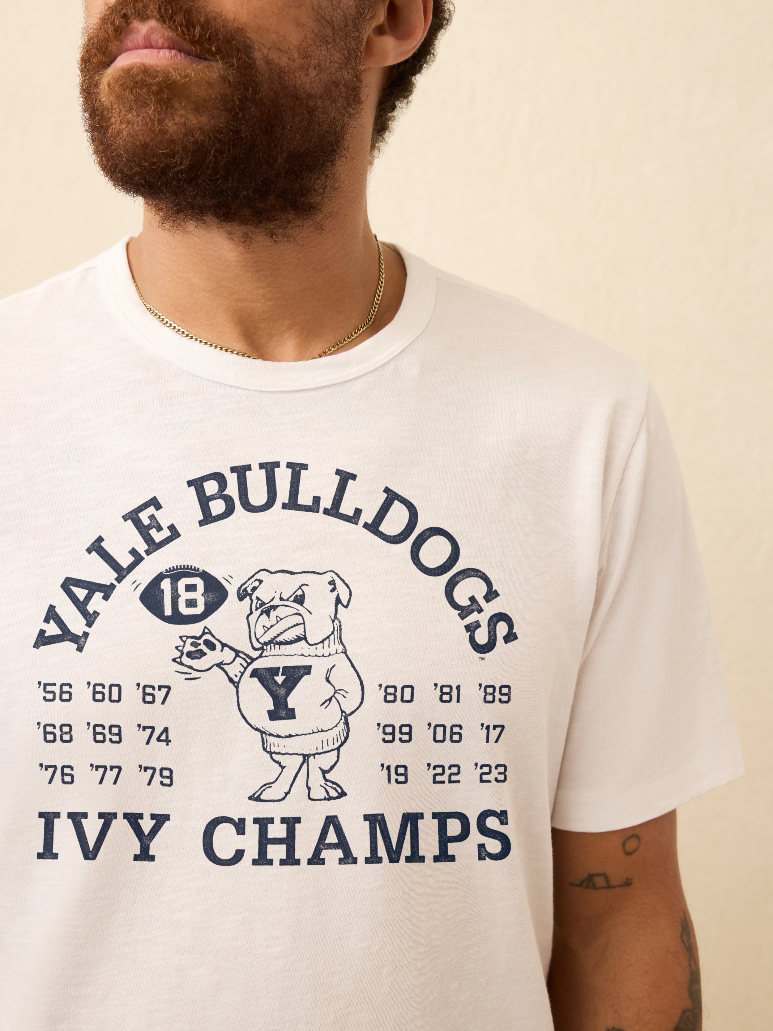 Man wearing a white t shirt with Yale graphic on the front against a beige background