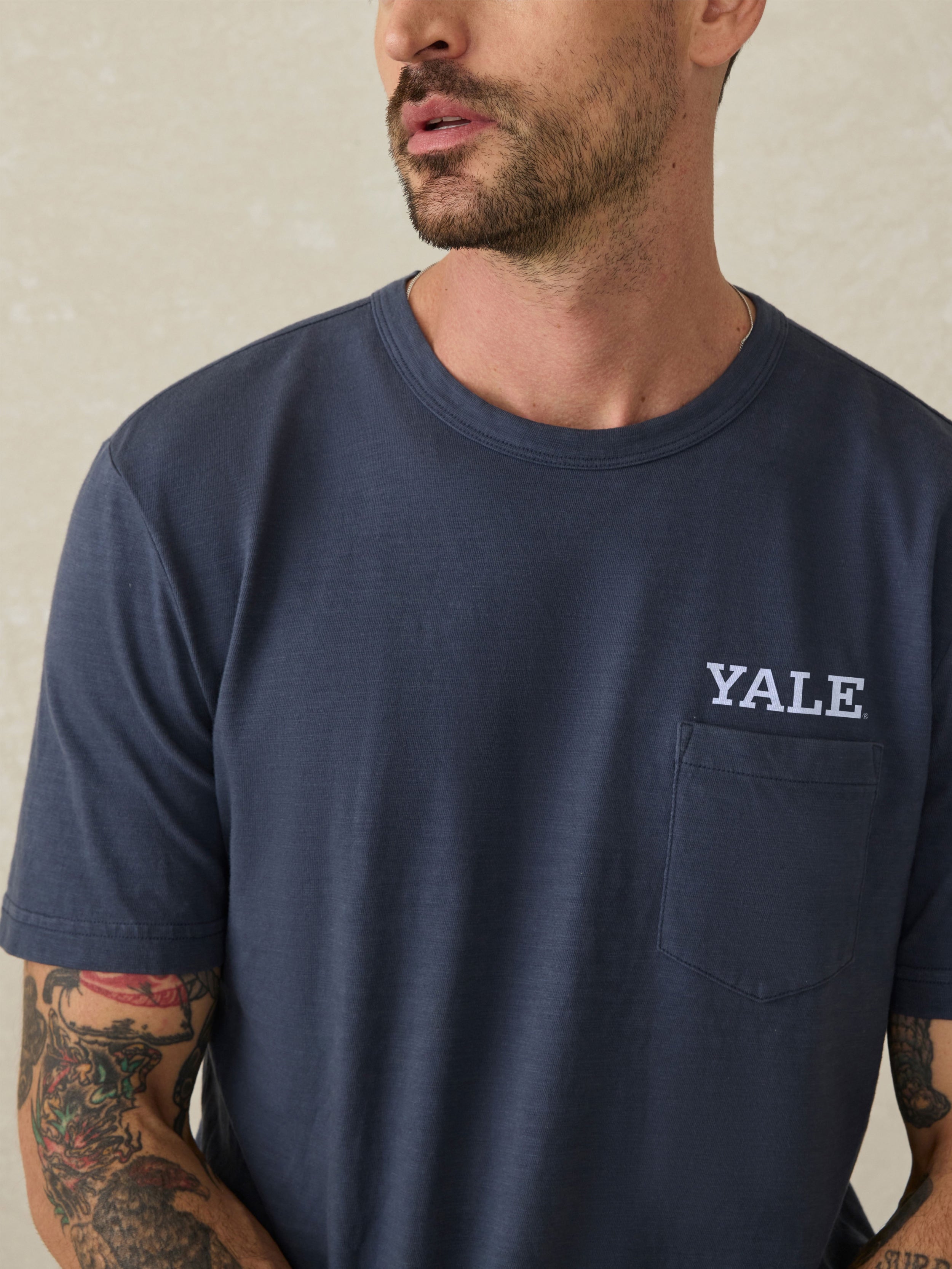 Man wearing a navy blue t-shirt with Yale graphic logo on a beige background