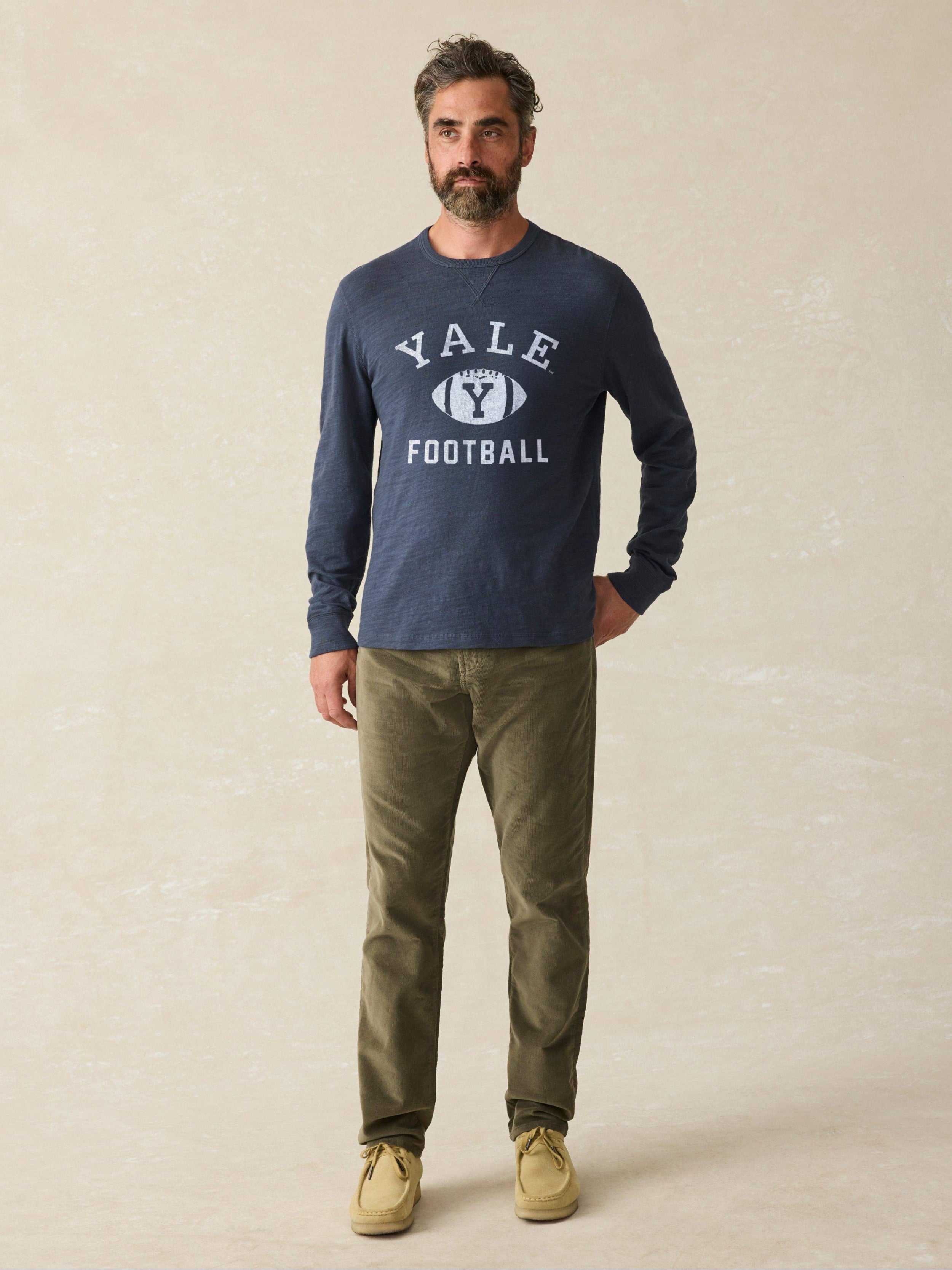 Man is wearing a navy long sleeve shirt with Yale graphic on chest against a beige background