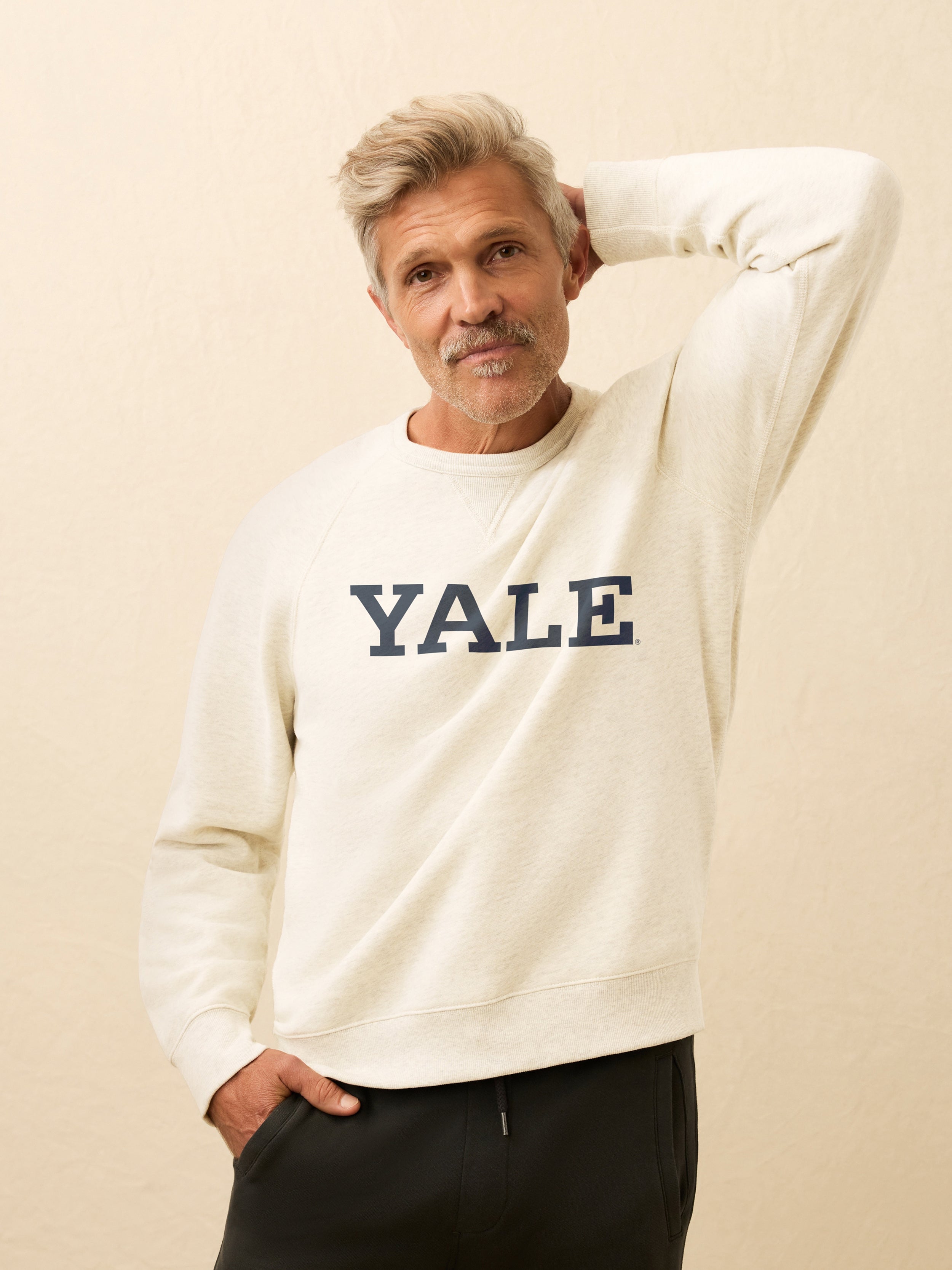 Man wearing a white sweatshirt with Yale graphic printed on it against a beige background