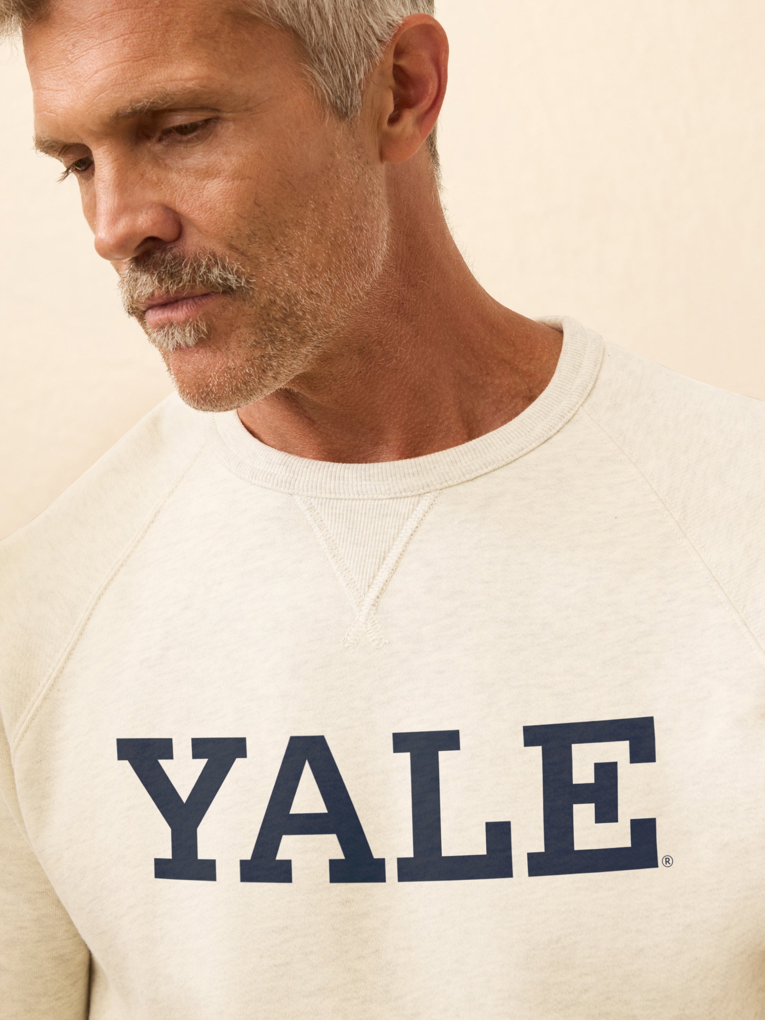 Man wearing a white sweatshirt with Yale graphic printed on it against a beige background
