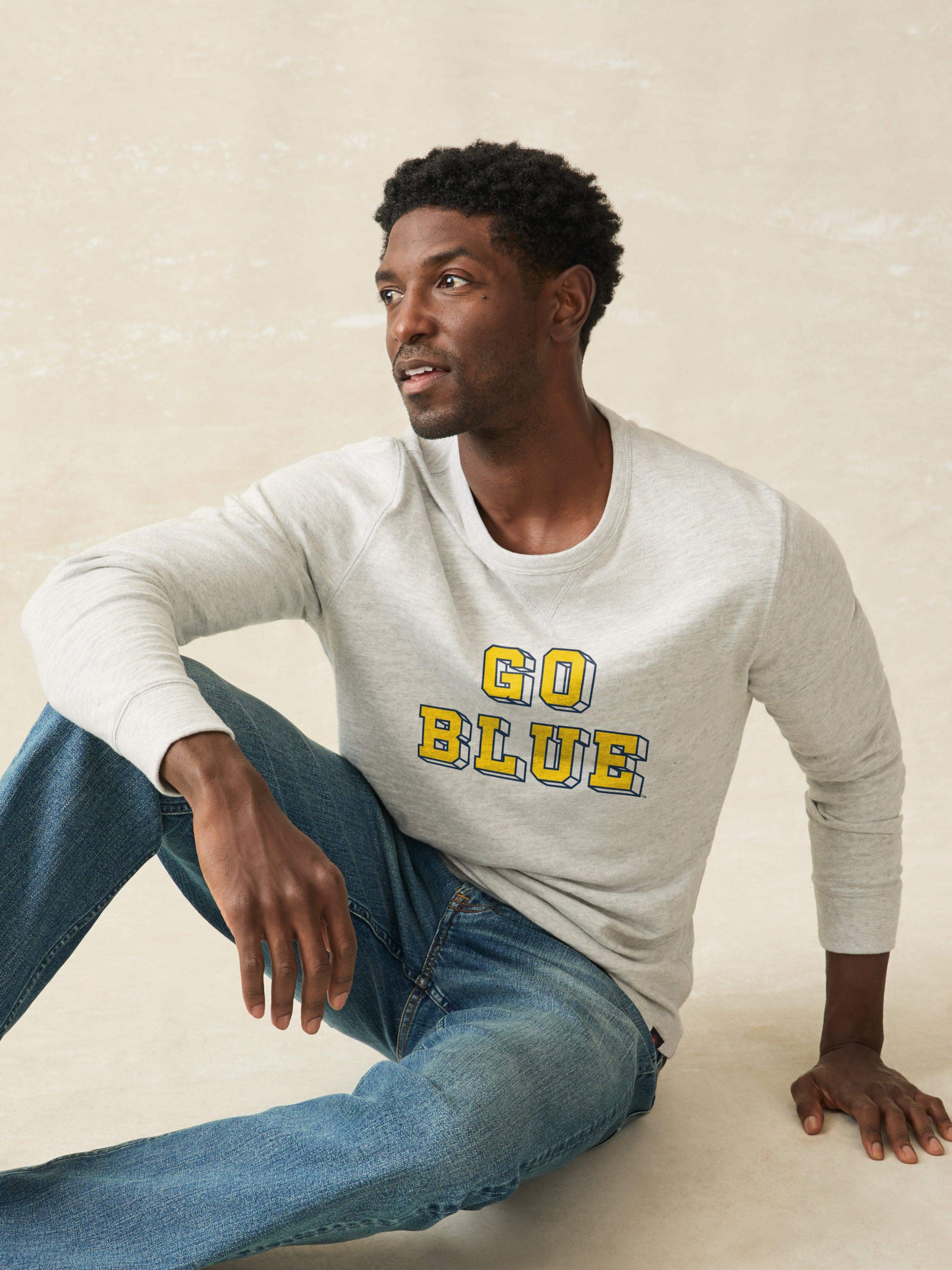 Man wearing a grey sweatshirt with Michigan graphic on the front against a beige background