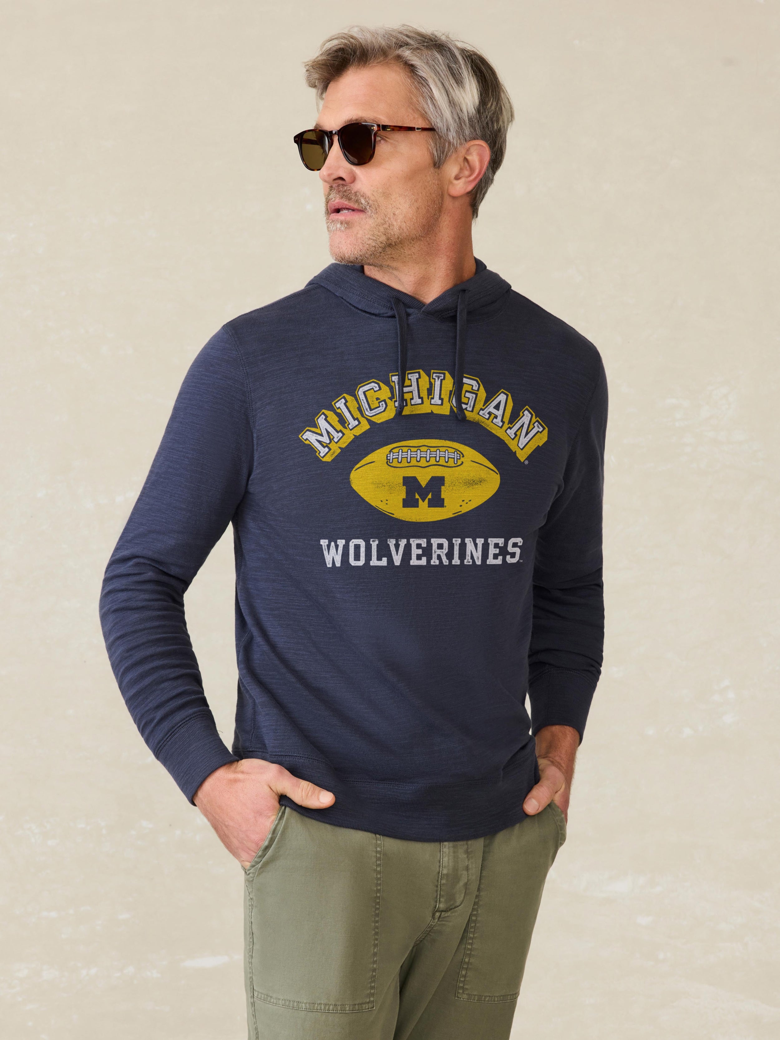Man wearing a navy hoodie with a Michigan graphic against a beige background
