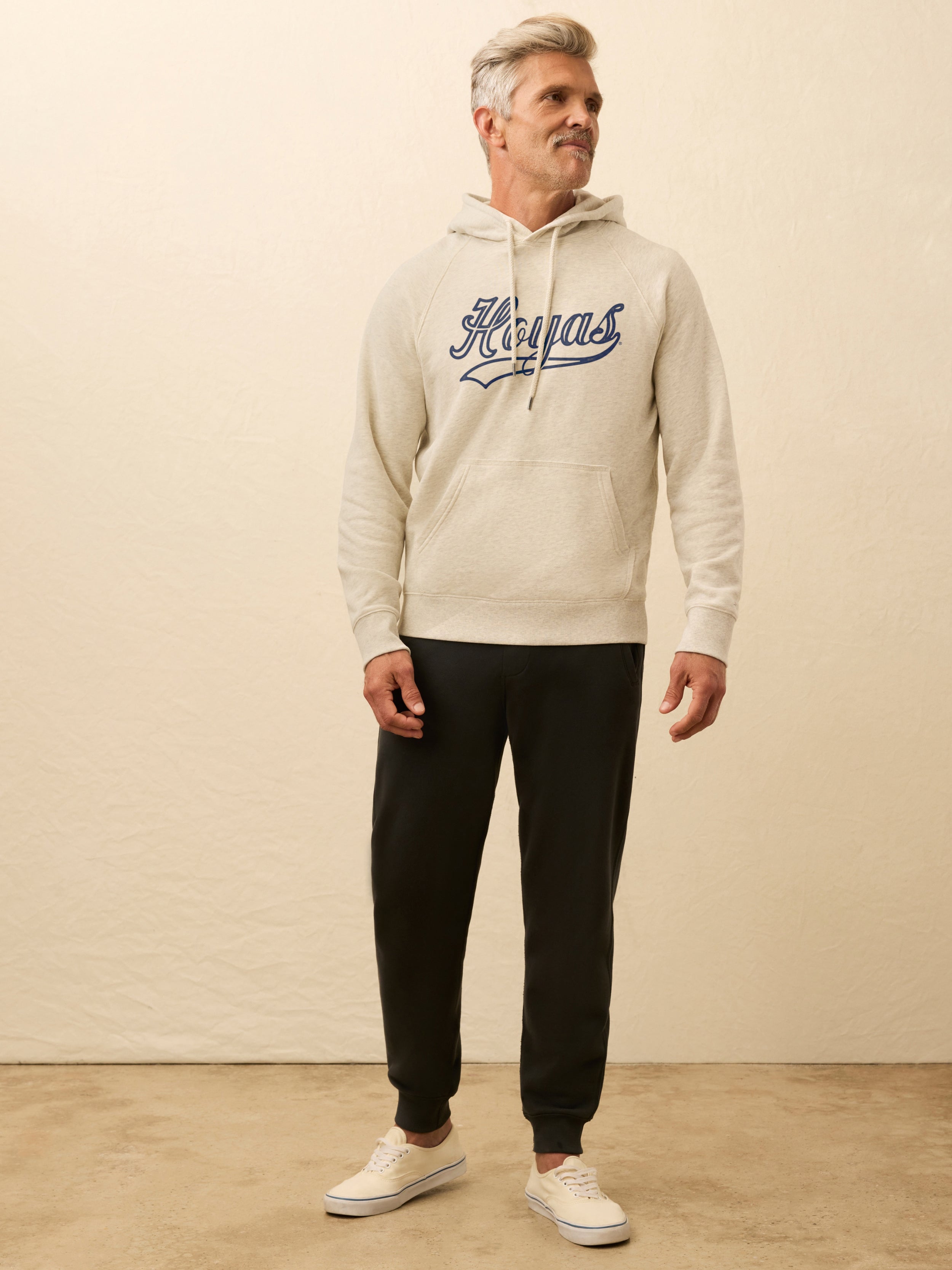 Man wearing an ivory heather hoodie with Georgetown graphic on the center chest against a beige background