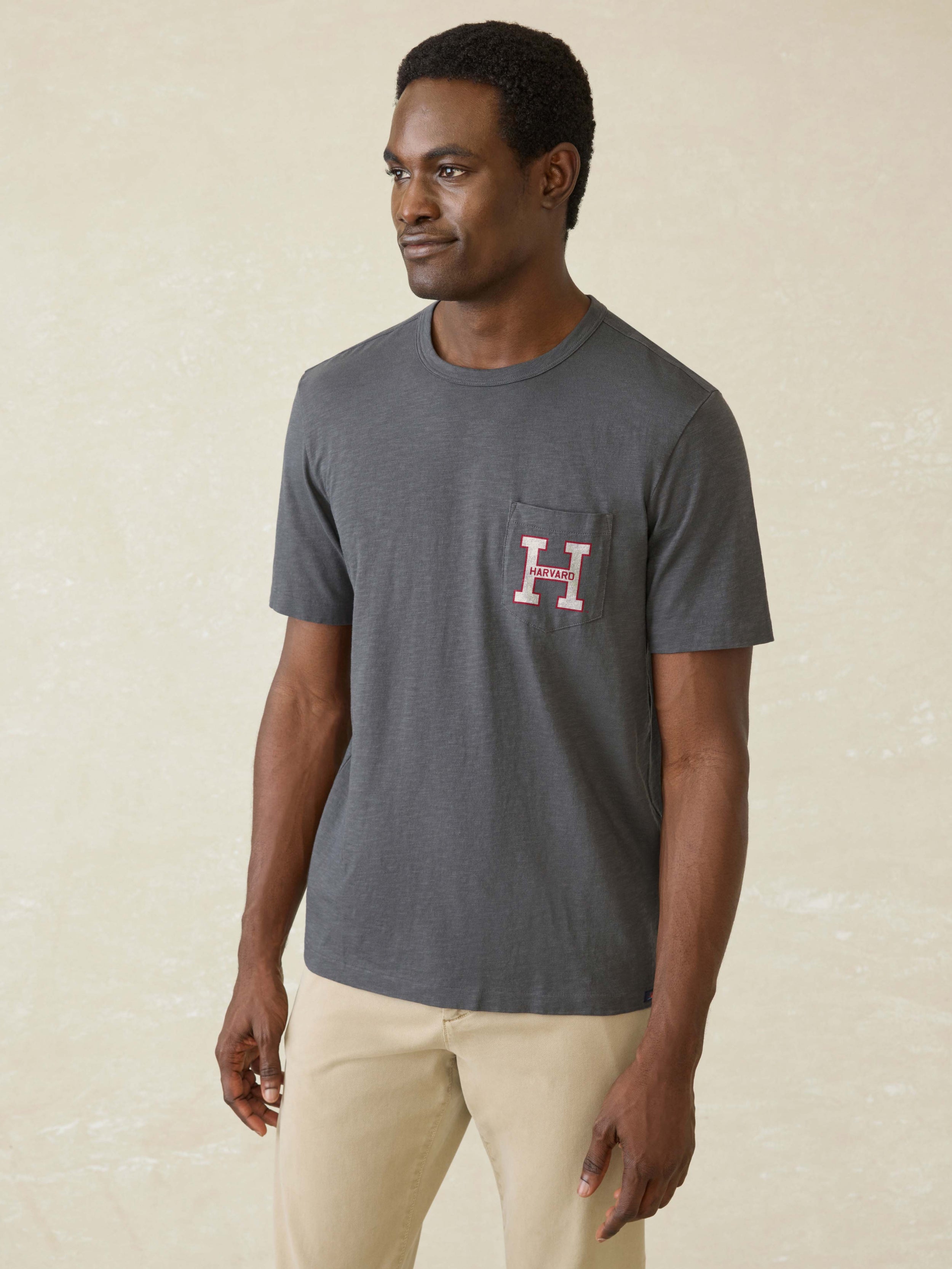 Man wearing a gray t-shirt with Harvard graphic on front left chest pocket against a beige background
