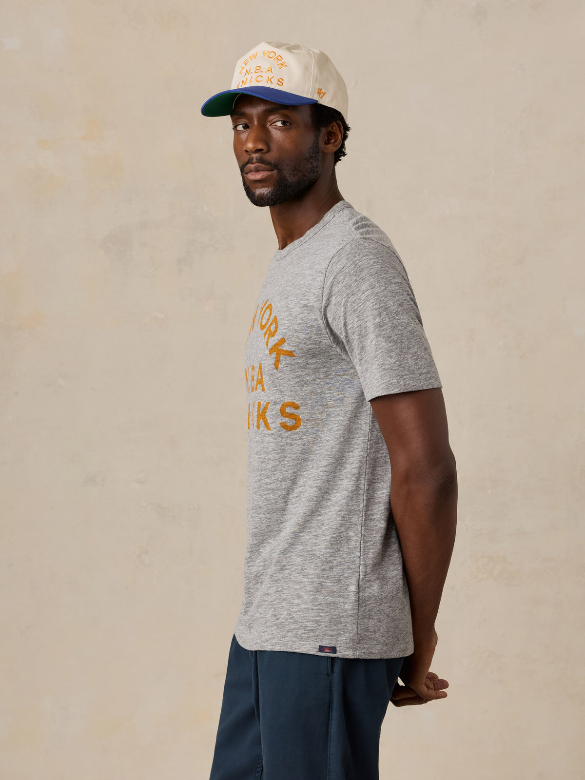 A man wearing a grey NY Knicks tee and hat, image 5 of 6