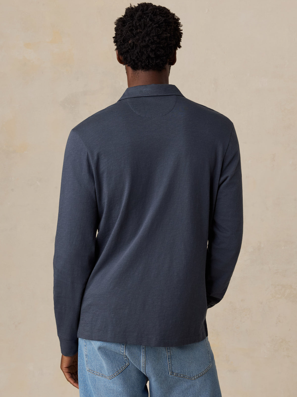 A man viewed from behind wearing a blue NY Knicks polo shirt, image 5 of 8