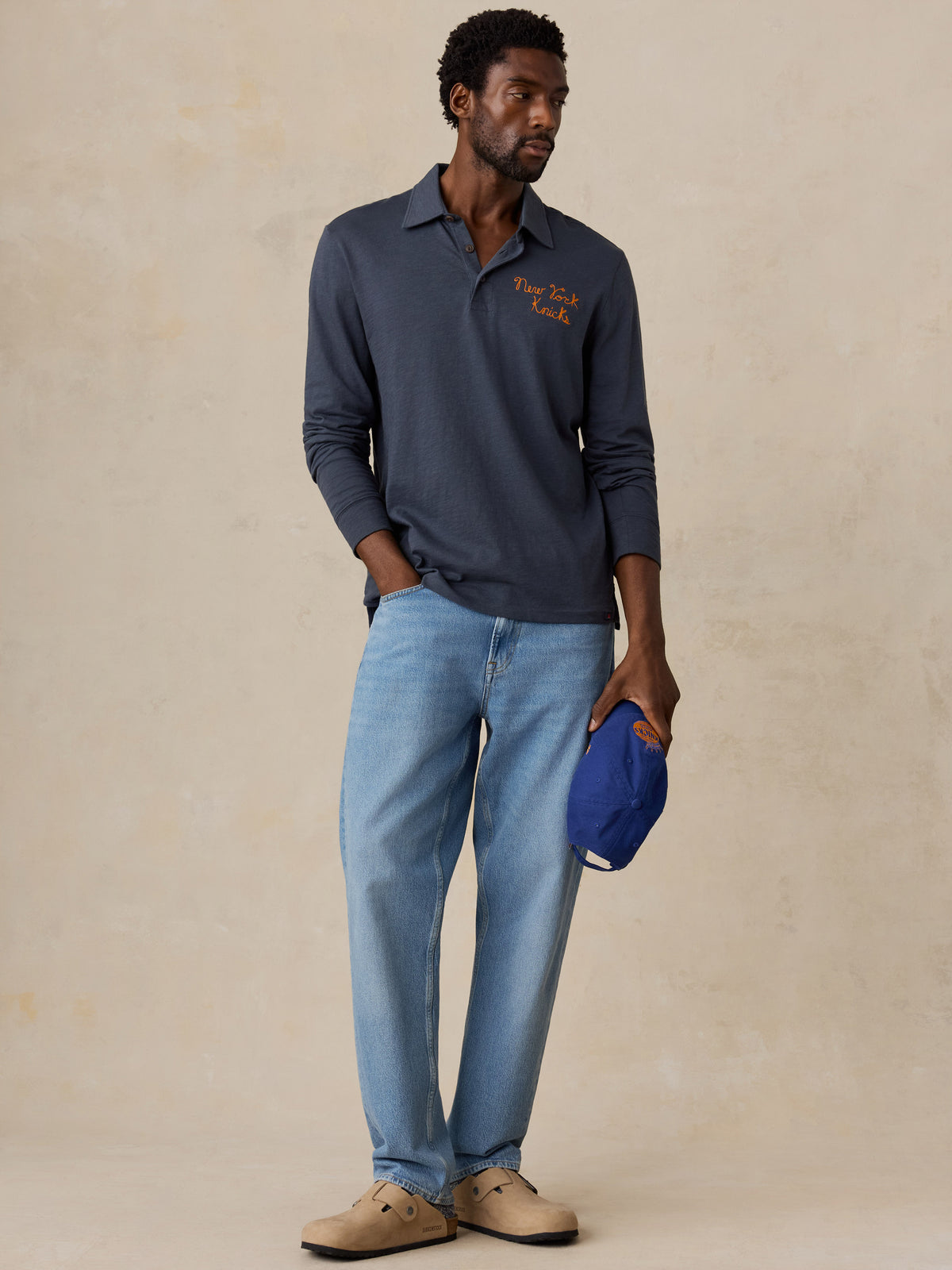 A man wearing a blue NY Knicks polo shirt and jeans, image 2 of 8