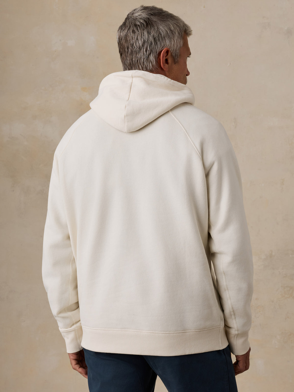A man viewed from behind wearing a white NY Knicks hoodie, image 3 of 6