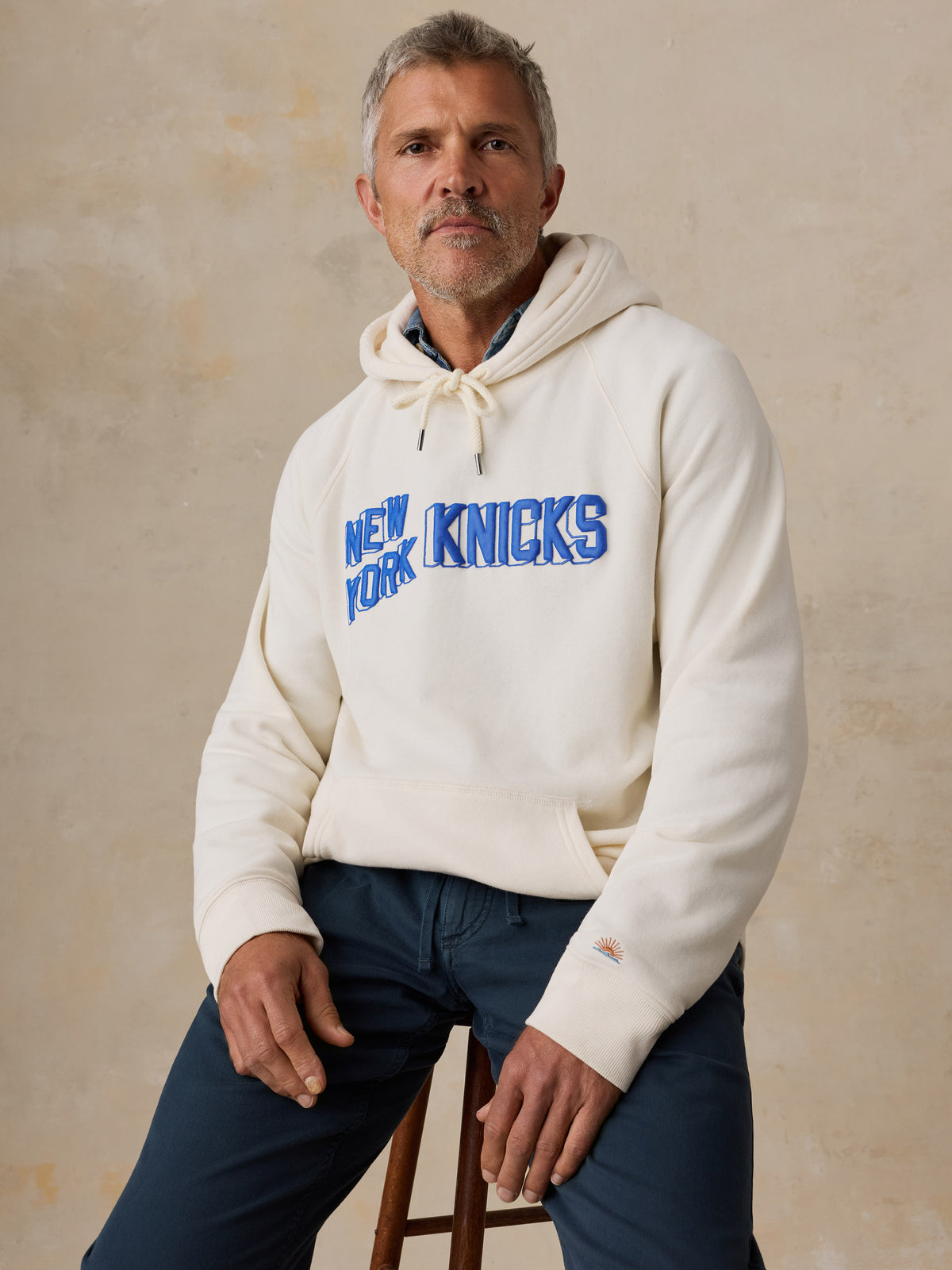 A man wearing a white NY Knicks hoodie and blue pants, image 5 of 6