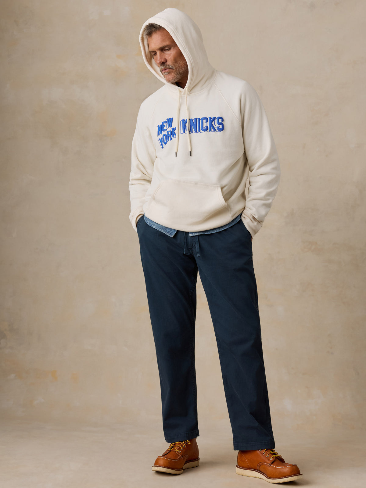 A man wearing a white NY Knicks hoodie and blue pants, image 2 of 6