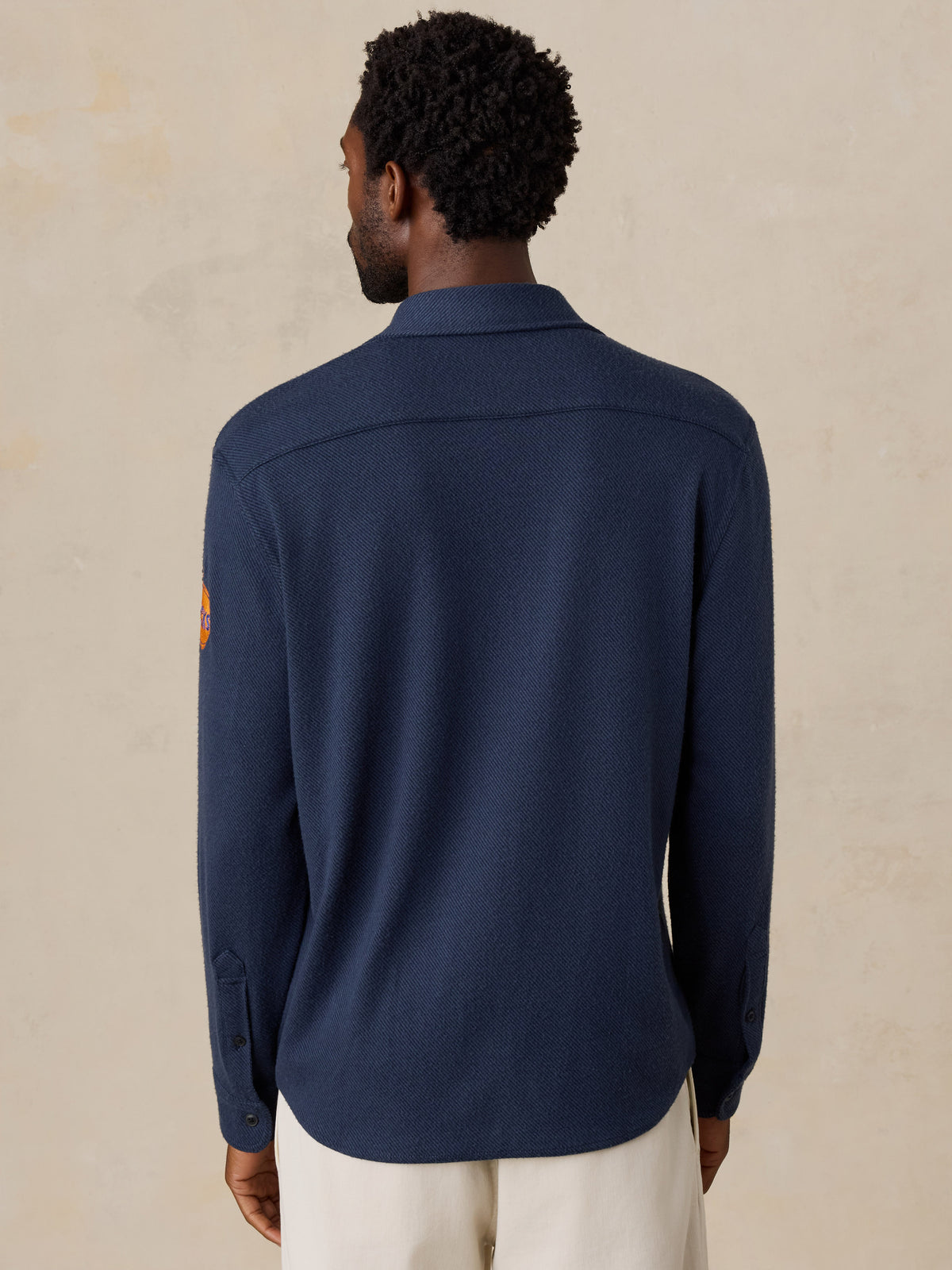 A man viewed from behind wearing a navy NY Knicks button up shirt, image 5 of 6