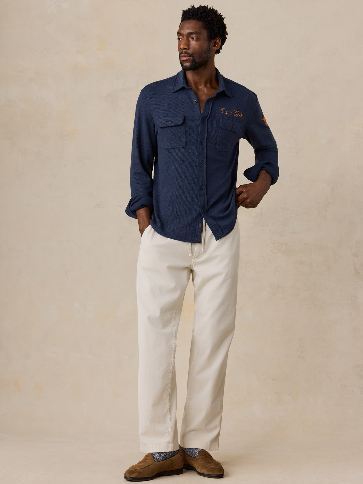 A man wearing a navy NY Knicks button up shirt and white pants, image 2 of 6