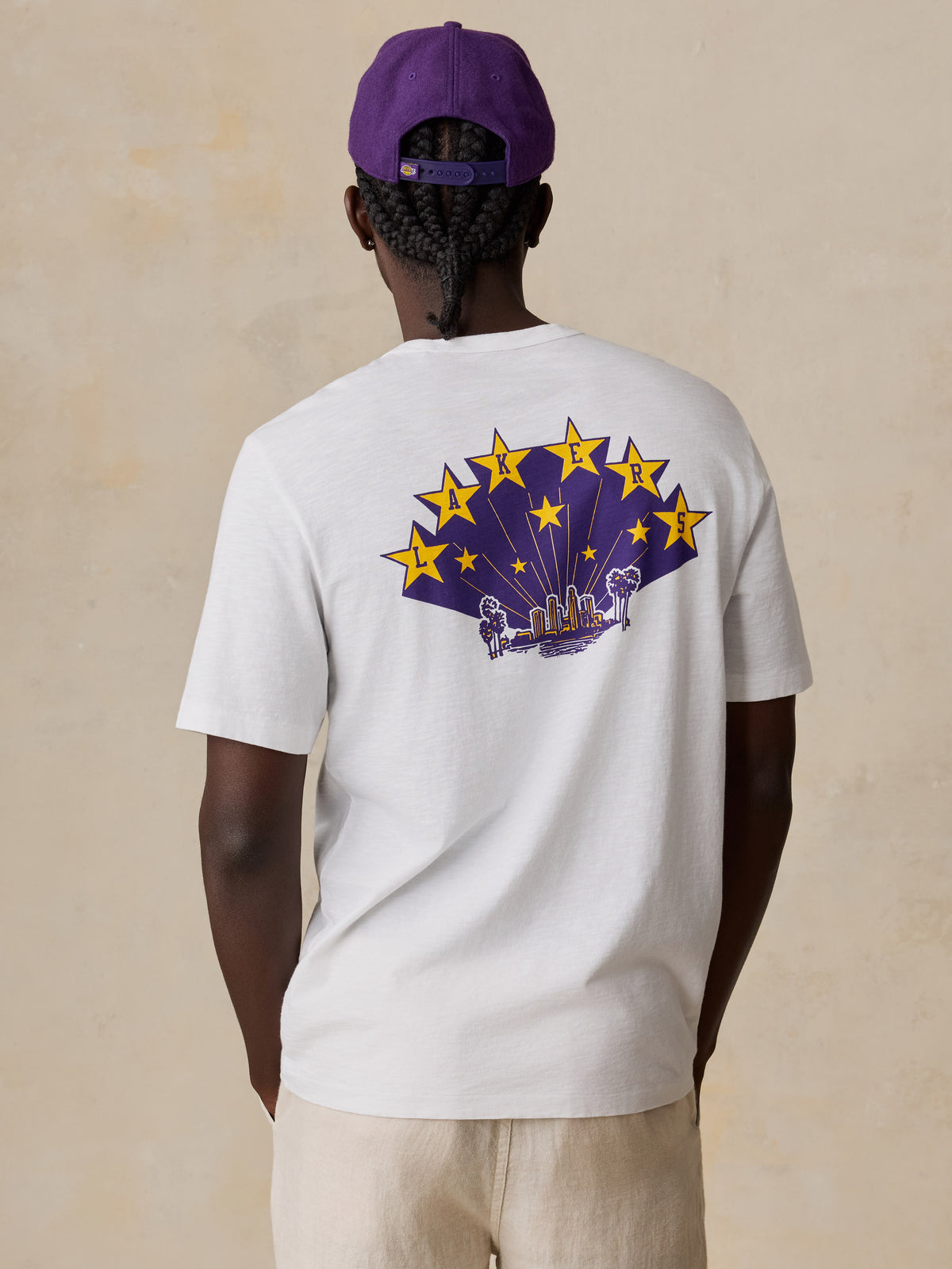A man viewed from behind wearing a white LA Lakers tee and linen pants, image 6 of 6