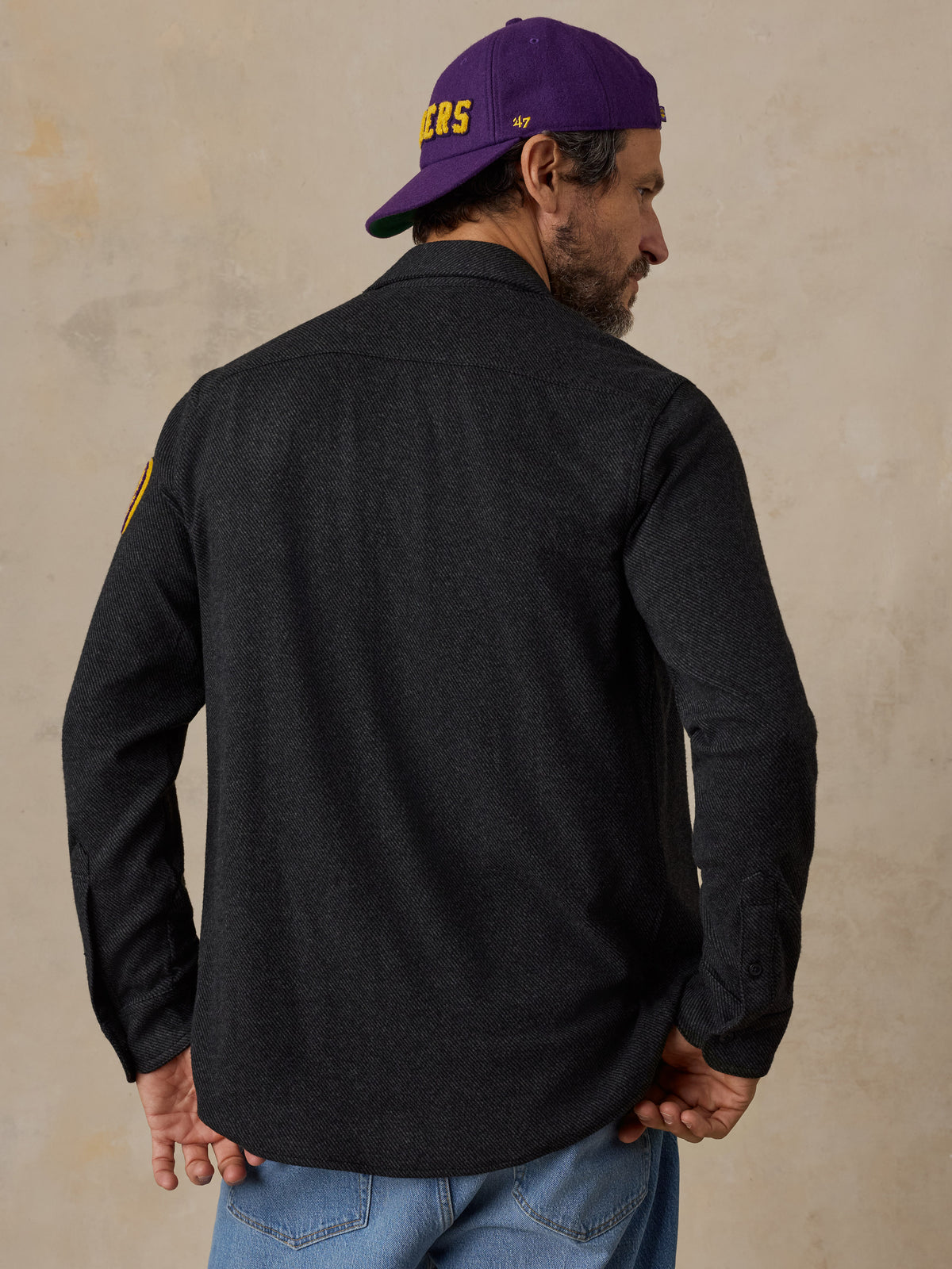 A man viewed from behind wearing a black LA Lakers shirt and blue jeans, image 3 of 6