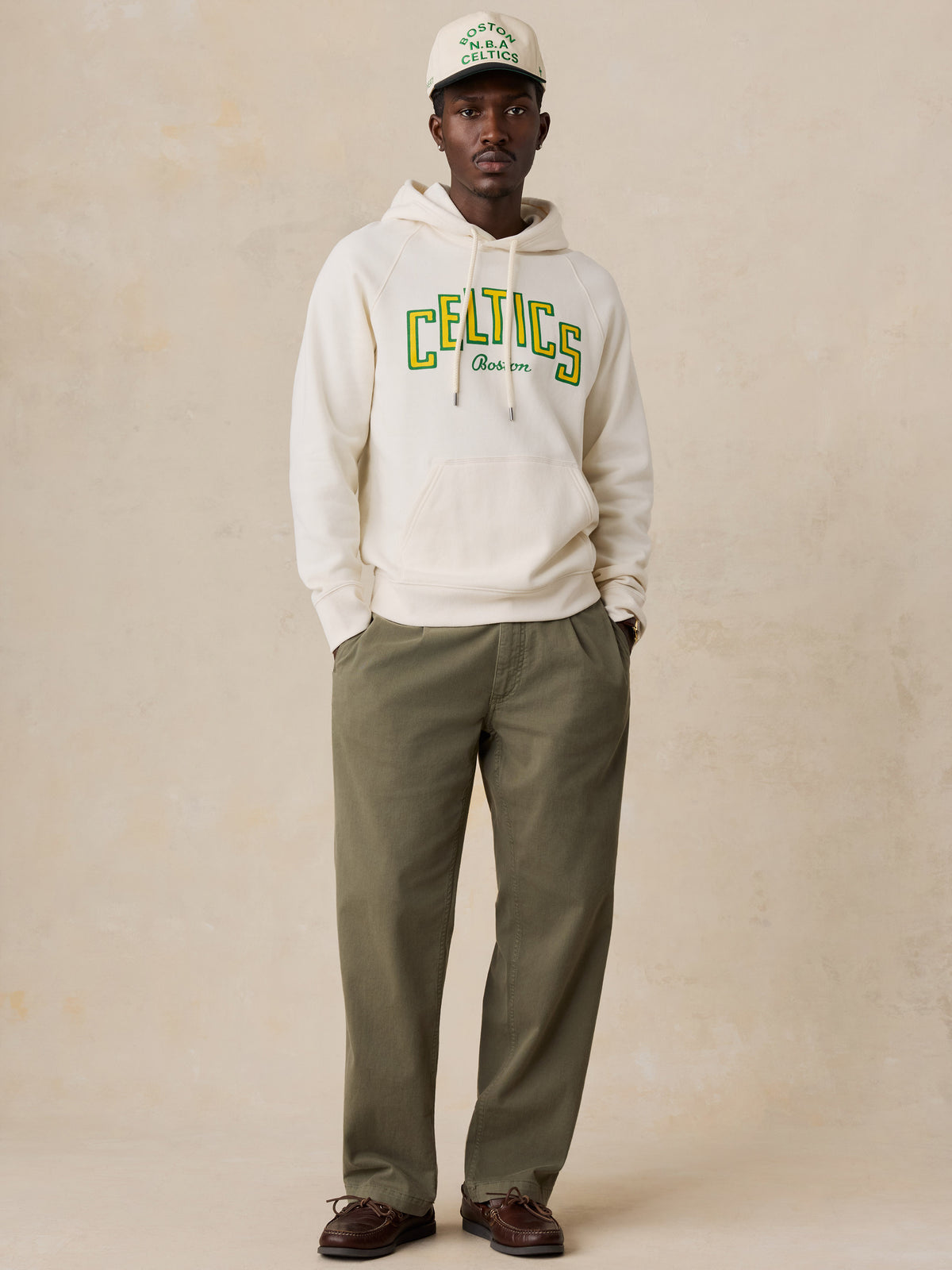 A man wearing a white Boston Celtics hoodie and green chinos, image 2 of 6