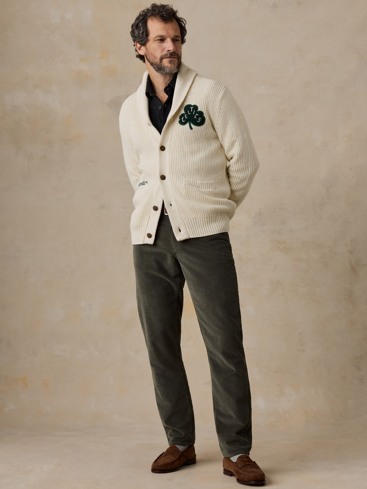 A man wearing an off-white Boston Celtics cardigan and green pants, image 3 of 7