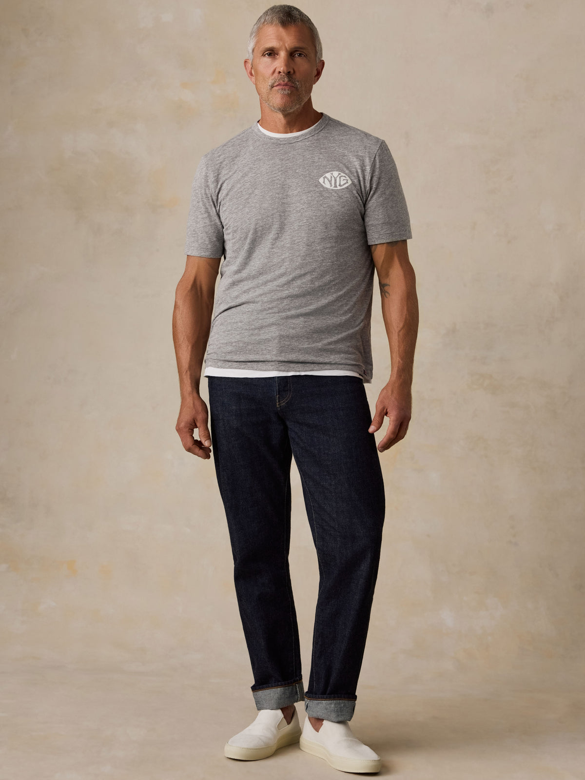 A man wearing a grey NY Giants t-shirt, blue jeans, and white sneakers, image 4 of 6