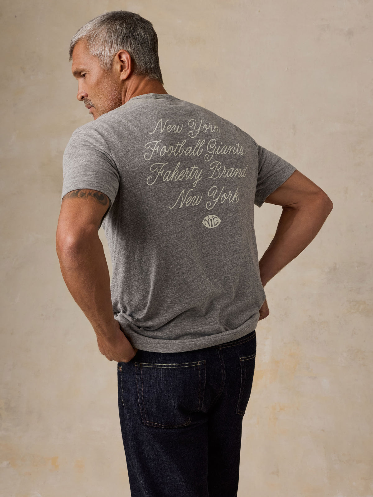 A man viewed from behind wearing a grey NY Giants t-shirt with blue jeans, image 6 of 6